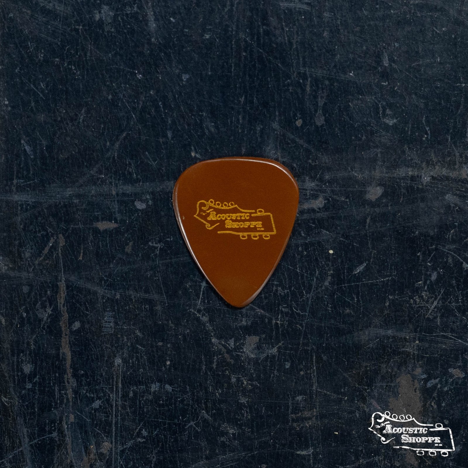 A BlueChip Picks (TD50) teardrop guitar pick by BlueChip, featuring an Acoustic Shoppe and guitar graphic, rests on a dark textured surface. The Acoustic Shoppe logo is displayed in the bottom right corner.