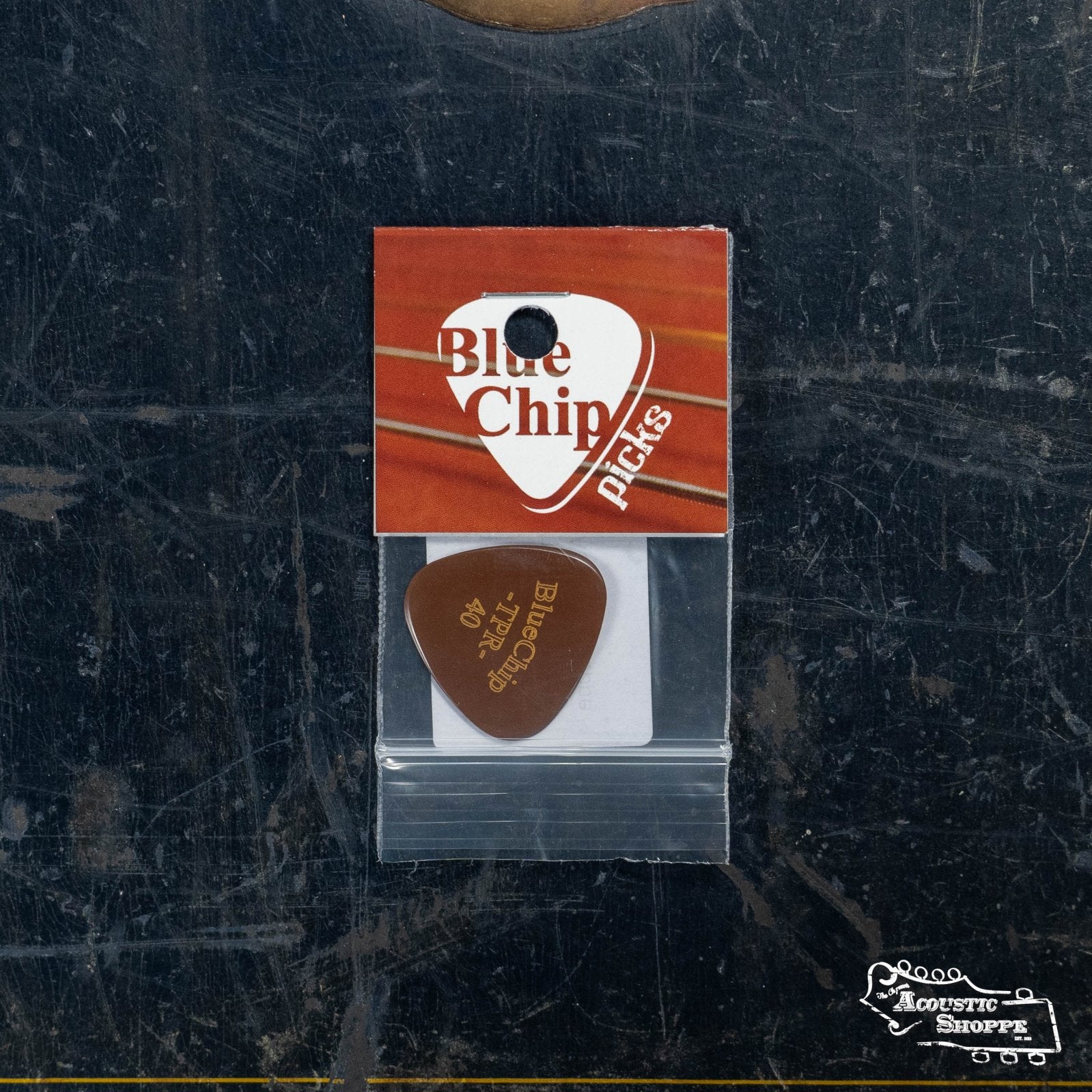 A BlueChip Picks (TPR40) guitar pick by BlueChip is shown in a clear plastic bag with a red and white label, resting on a dark, worn surface featuring the Acoustic Shoppe logo in the corner.