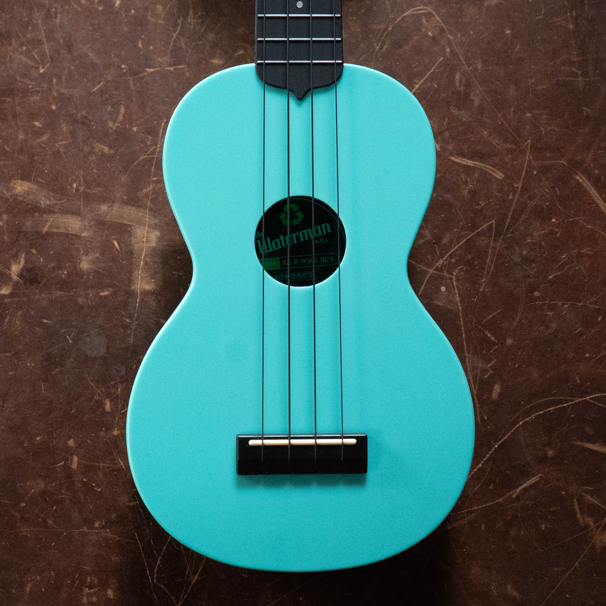 Aqua mist blue soprano ukulele with black bridge, fretboard, and soundhole label on wooden surface. - The Waterman Aqua Mist Glow-In-The-Dark Soprano Recycled Ukulele - Kala Brand - Default Title