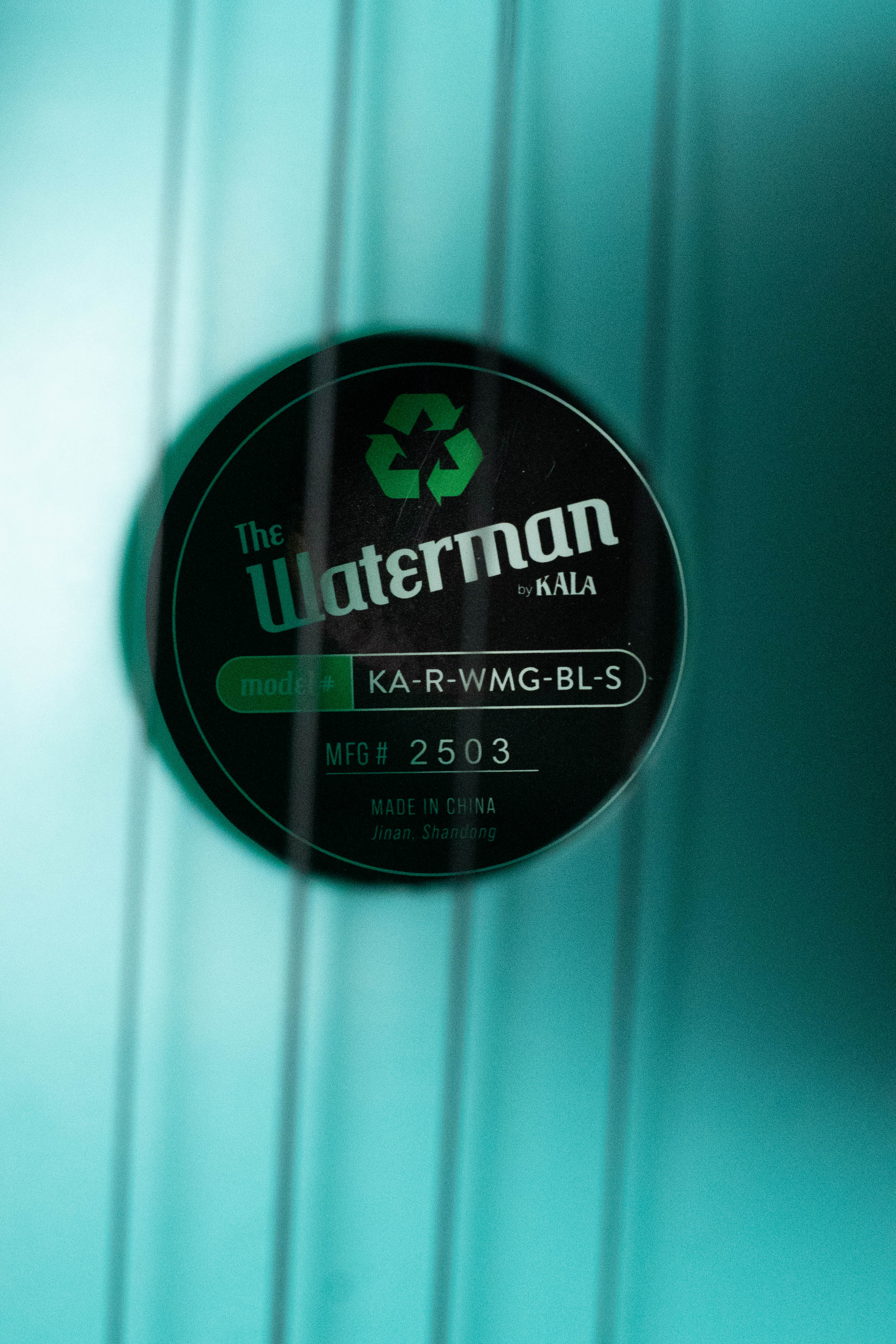 Close-up of the Waterman Aqua Mist recycled soprano ukulele's label with a green glow-in-the-dark finish and black text. - The Waterman Aqua Mist Glow-In-The-Dark Soprano Recycled Ukulele - Kala Brand - Default Title