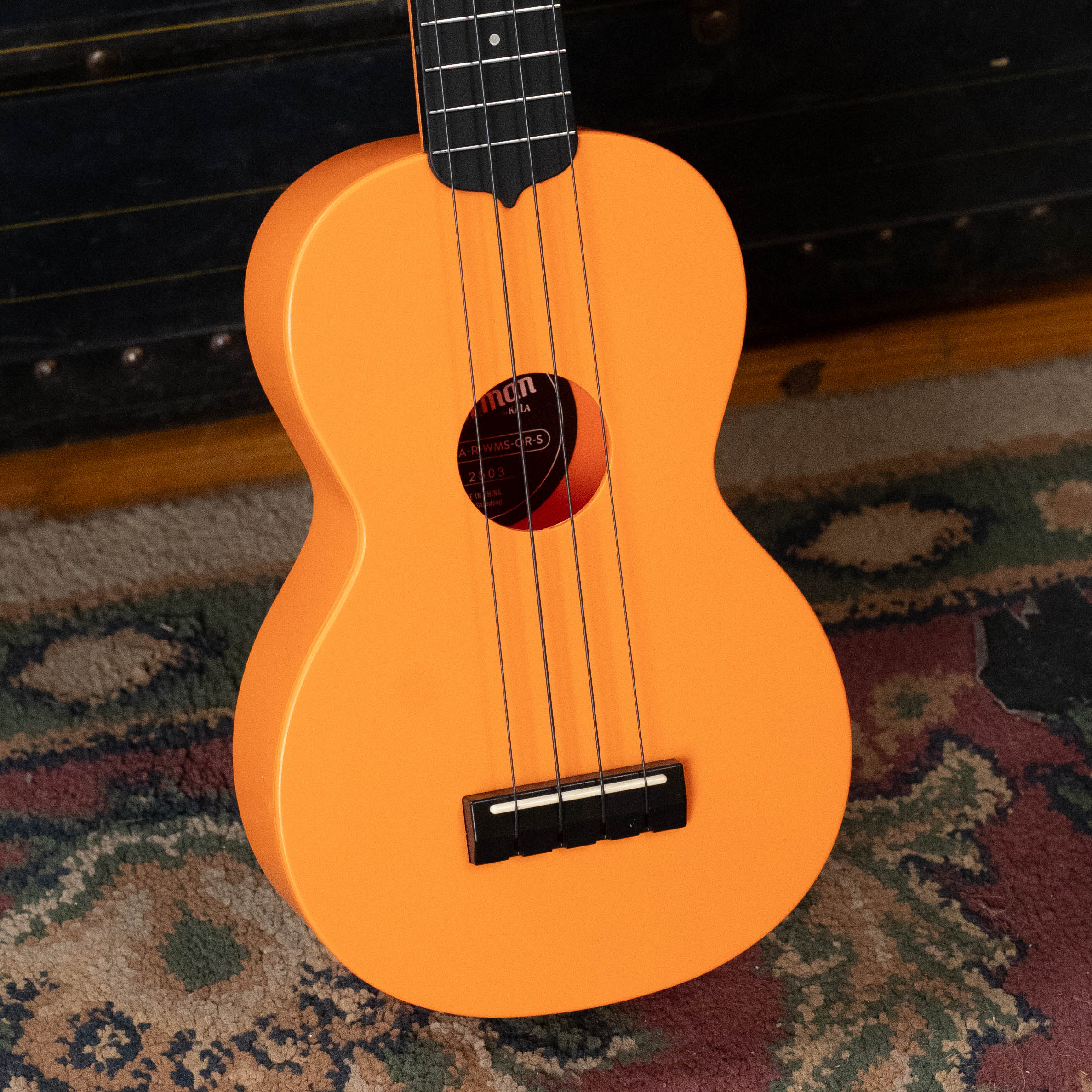 Sunset orange soprano ukulele with black fretboard and bridge on patterned rug background. - The Waterman Sunset Orange Soprano Recycled Ukulele - Kala Brand - Default Title