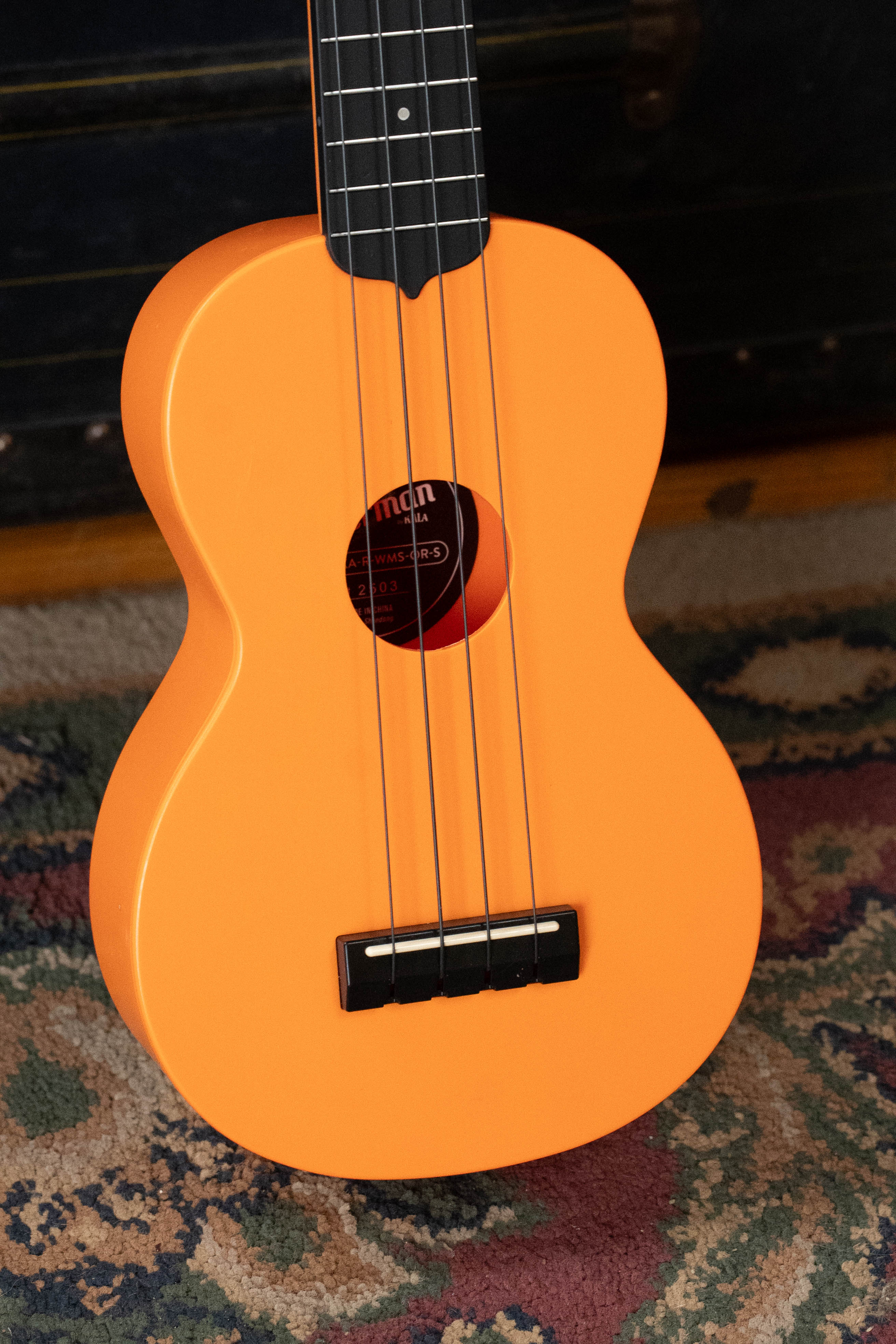 Sunset orange soprano ukulele with black tuning pegs and bridge on patterned rug. - The Waterman Sunset Orange Soprano Recycled Ukulele - Kala Brand - Default Title