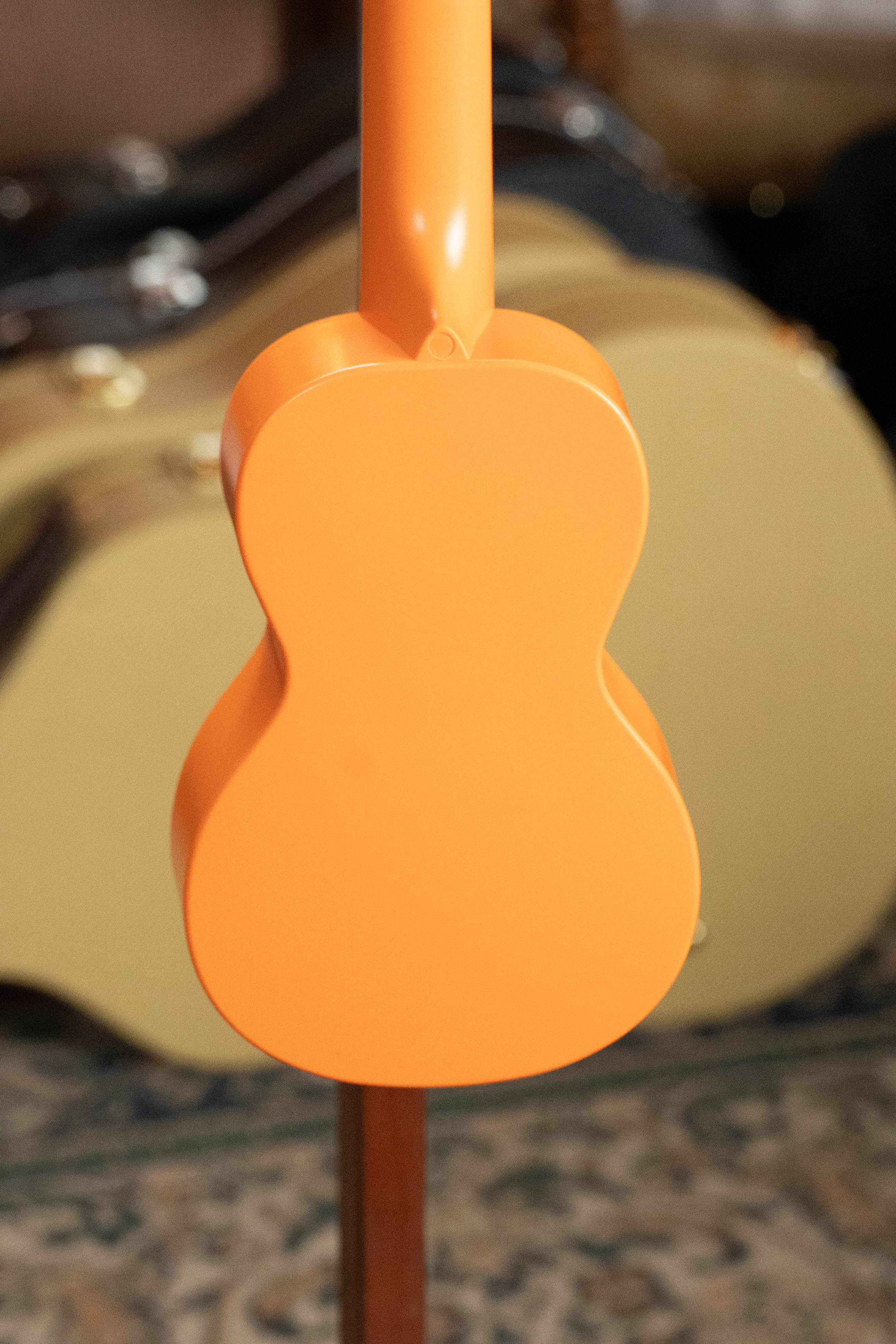Sunset orange soprano ukulele with smooth matte finish and rounded edges on a stand. - The Waterman Sunset Orange Soprano Recycled Ukulele - Kala Brand - Default Title