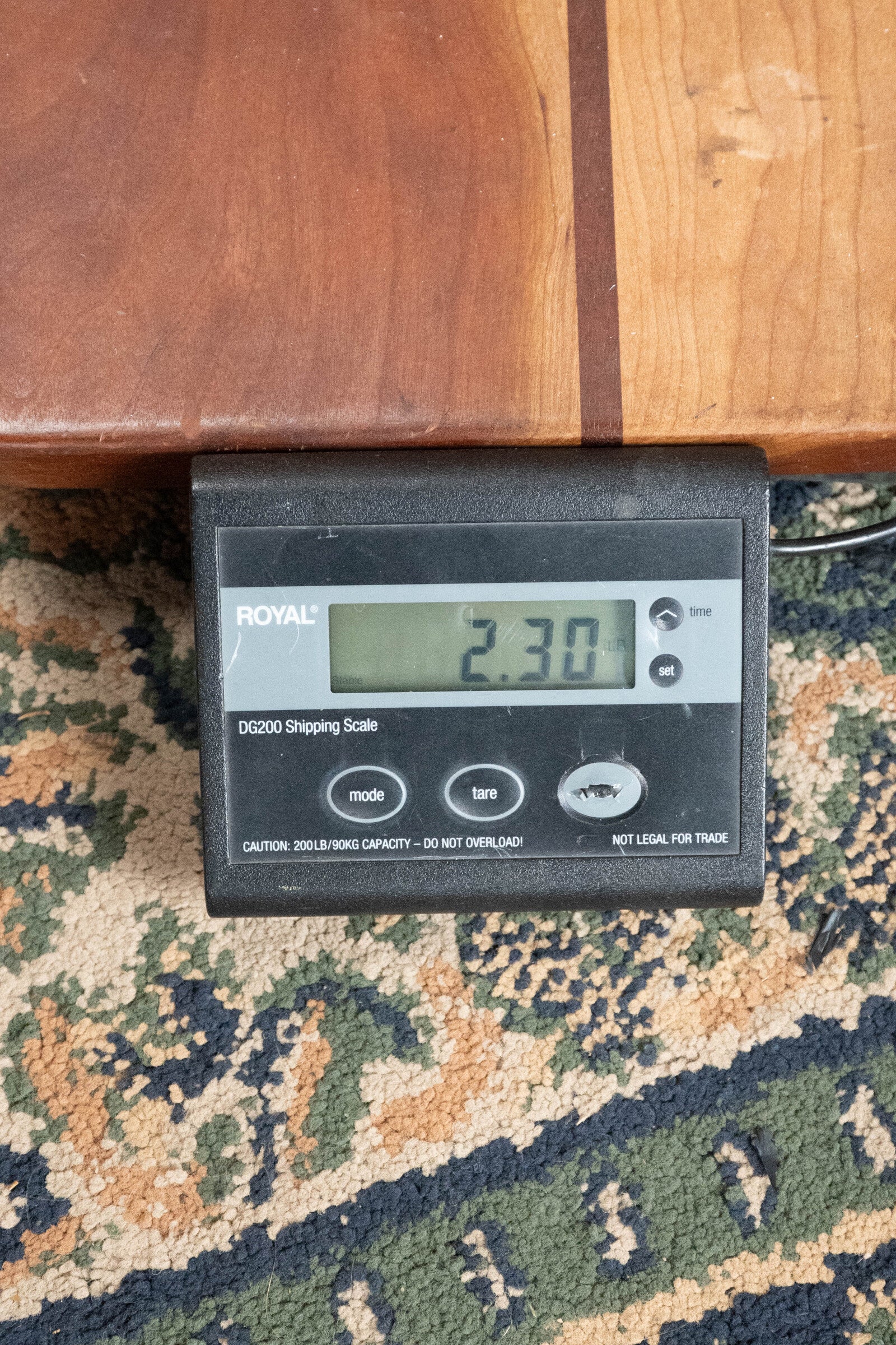 A digital shipping scale on a patterned carpet shows 2.30 lbs, with The Loar LM-310F-BRB Honey Creek F-Style Brownburst Mandolin #0069 resting on a wooden board atop the scale.