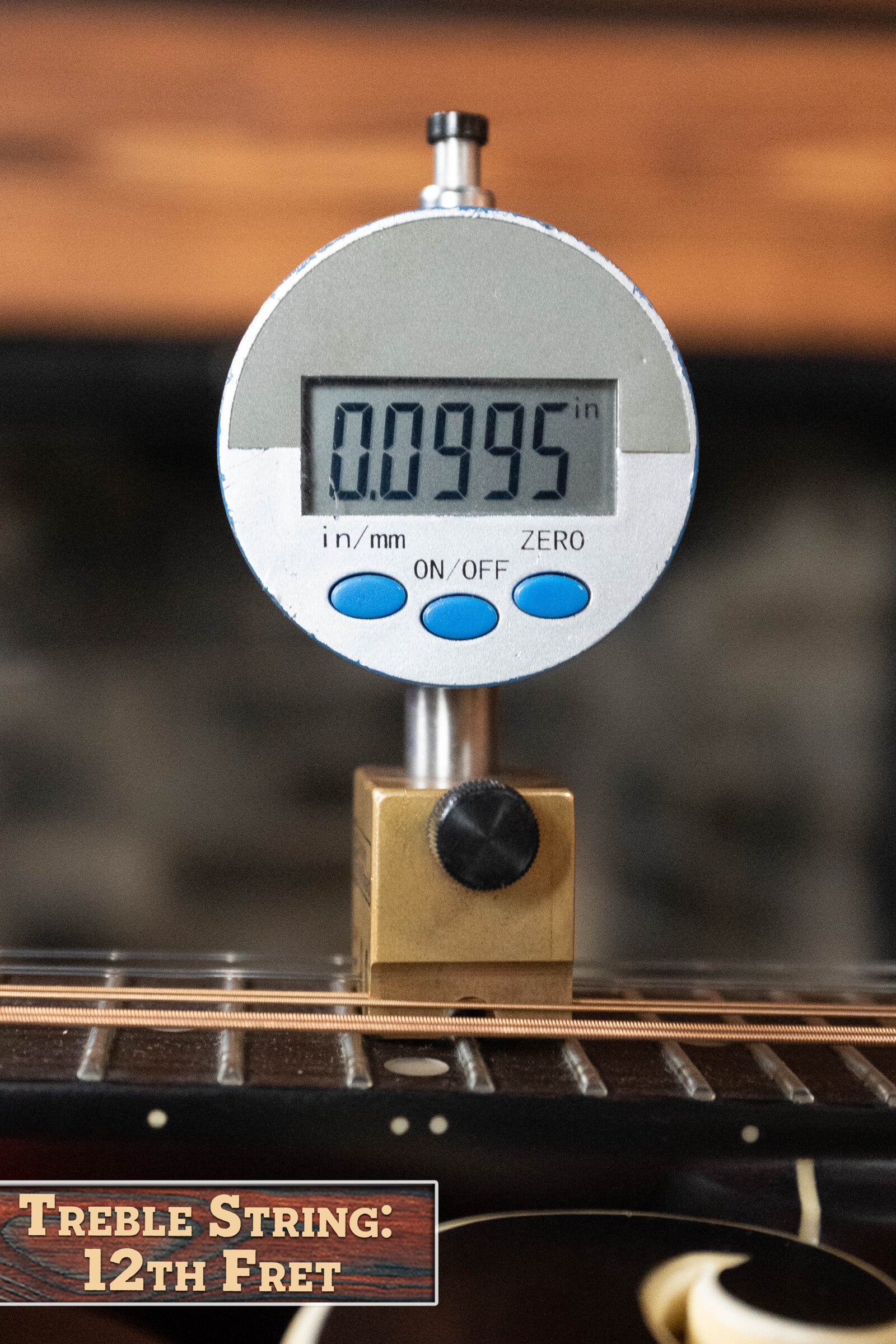 A digital gauge on a guitar neck reads 0.0995 inches at the 12th fret, similar to precise setups of The Loar LM-310F-BRB Honey Creek F-Style Brownburst Mandolin #0069. Text at the bottom left says: “Treble String: 12th Fret.”.
