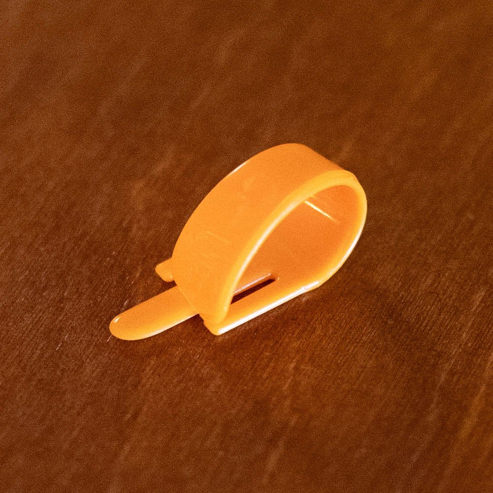 A Fred Kelly D3M Speed Single Orange Pick by Fred Kelly rests on a brown wooden surface, beside a silver 3-pin male XLR connector.
