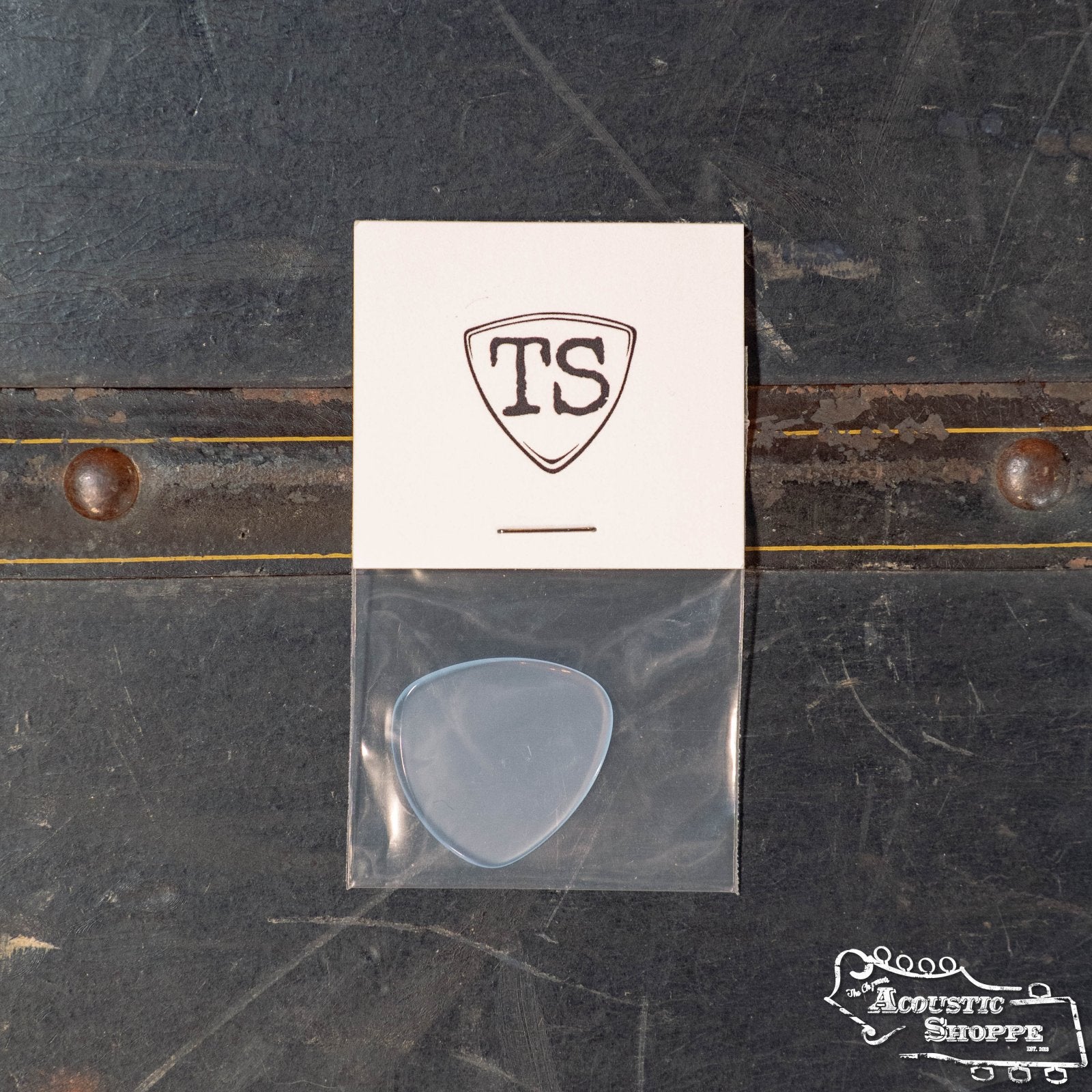 A white card with the TS logo and a ToneSlabs Oh Seven Rounded Jazz Guitar Pick (1.4 mm) sits in a plastic bag on a dark surface with metallic details; The Acoustic Shoppe logo appears in the bottom right corner.