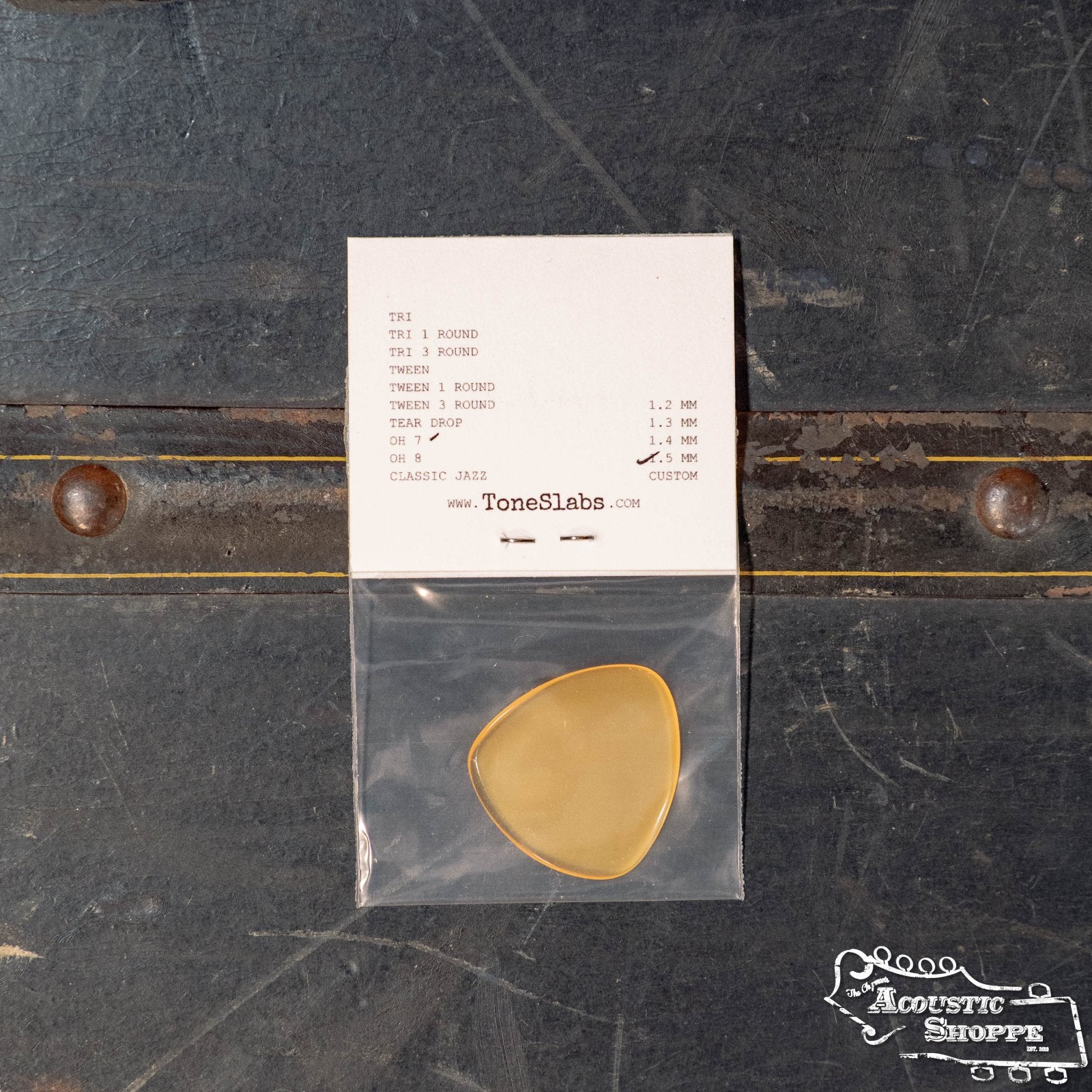 A ToneSlabs Oh Seven Rounded Jazz Guitar Pick (1.5 mm) in yellow is shown in a clear bag on a dark surface, with an info card above and “Acoustic Shoppe” branding at the bottom right.