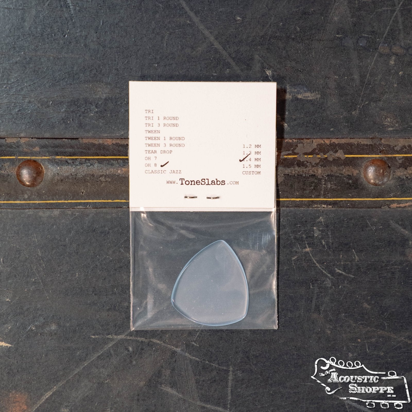 A ToneSlabs Oh Eight Pointed Jazz Guitar Pick (1.4 mm) by ToneSlabs is in a plastic bag attached to a branded info card, shown on a dark textured surface with visible screws and The Acoustic Shoppe logo at the bottom right.
