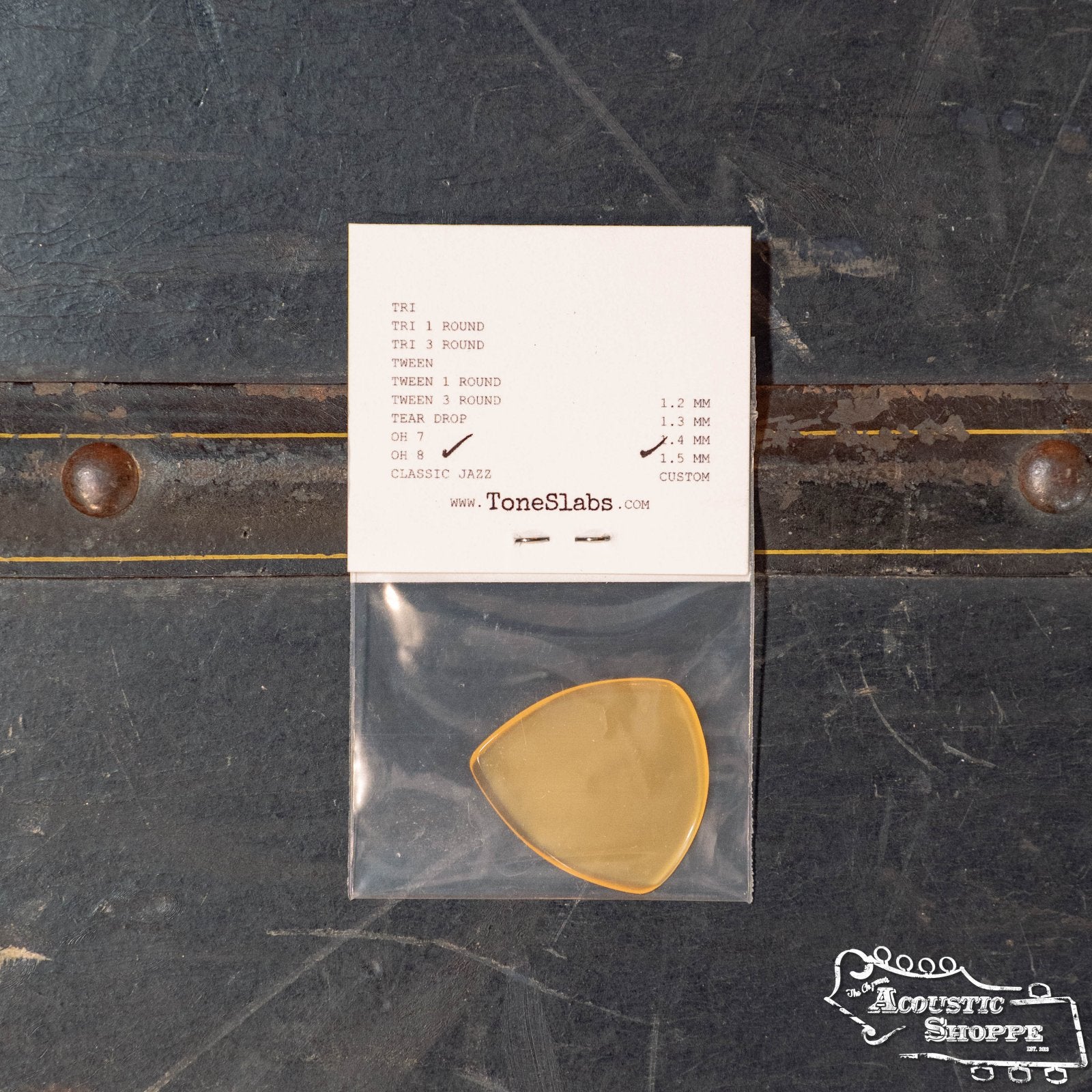A ToneSlabs Oh Eight Pointed Jazz Guitar Pick - 1.5 mm in yellow sits in a clear bag below a ToneSlabs info card on a dark surface, with The Acoustic Shoppe logo at the lower right—a perfect choice to enhance your instrument's tone.