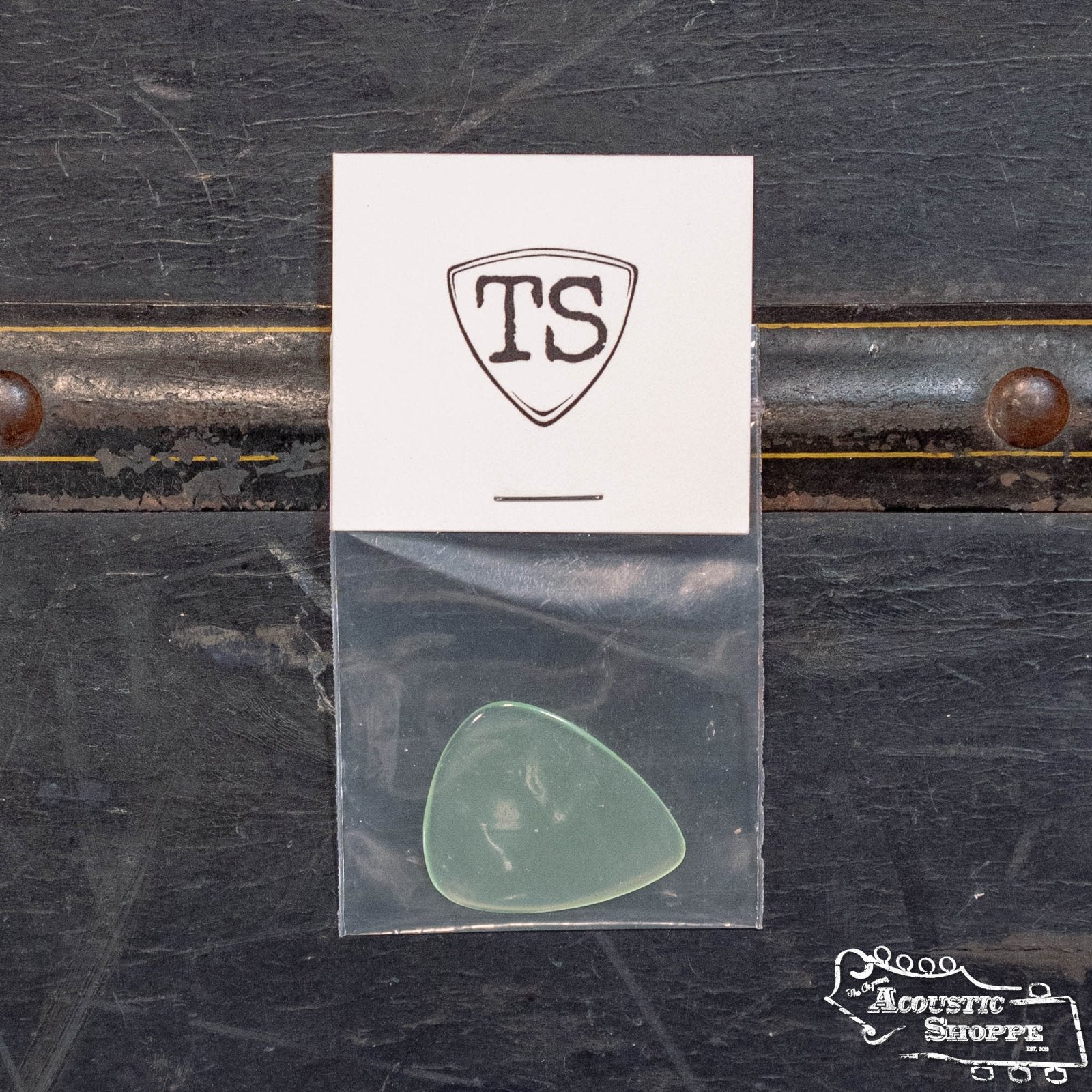 The ToneSlabs TAS Custom Tear Drop Guitar Pick - 1.3 mm (Exclusive Color) comes in a small plastic bag, shown below a white TS shield card on a dark surface with The Acoustic Shoppe logo in the corner.