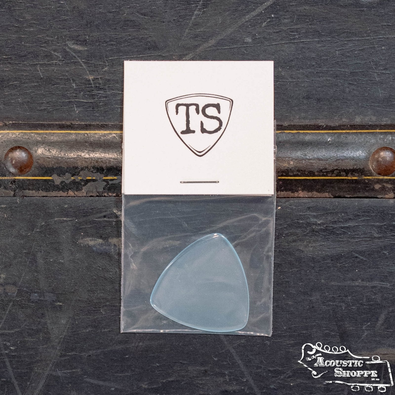 A translucent ToneSlabs XL Tri Corner Guitar Pick (1.4 mm) in a clear bag lies on a dark surface, with a white card above showing the TS shield logo. The Acoustic Shoppe logo appears at the bottom right.