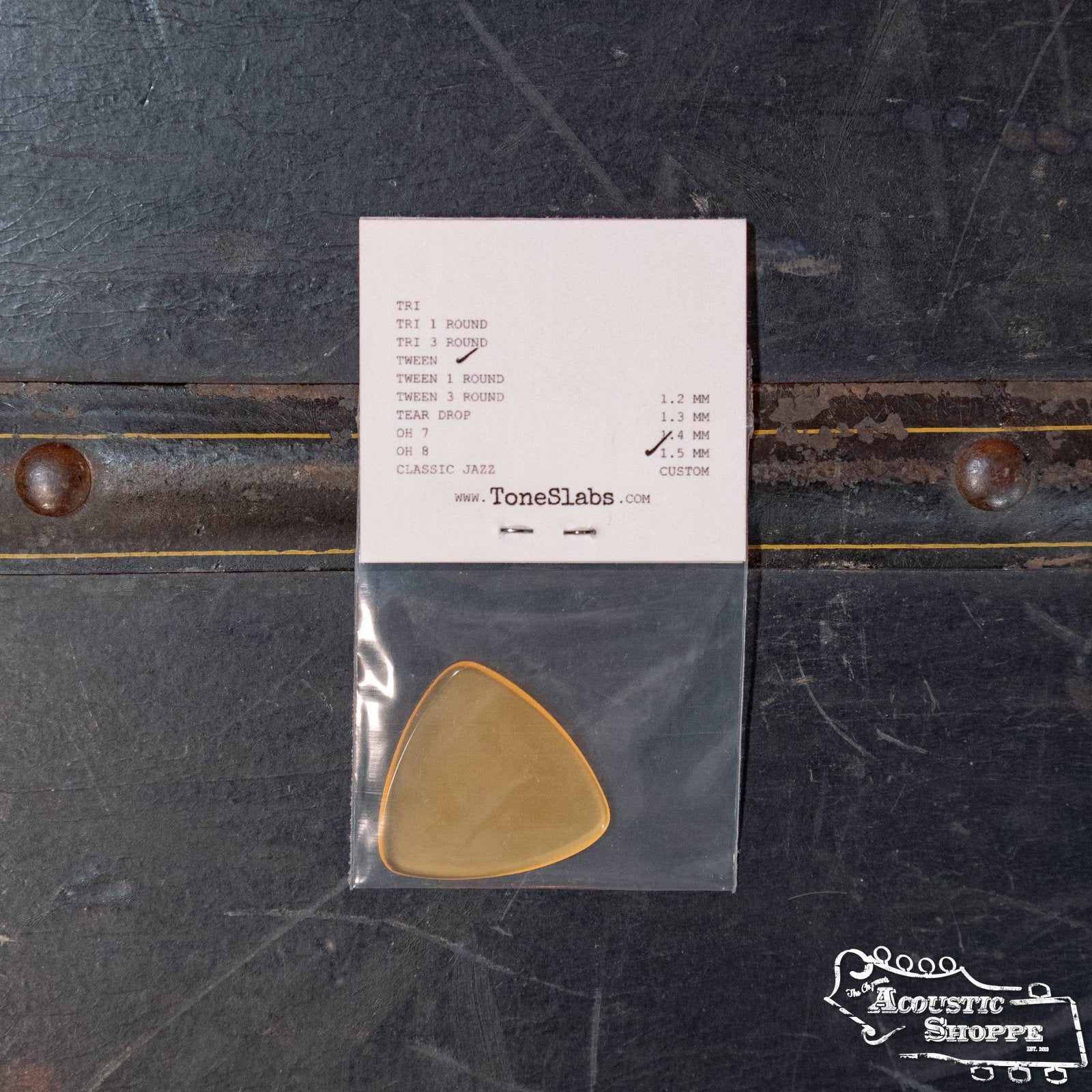 A ToneSlabs Tweener Triangle Guitar Pick - 1.5 mm by ToneSlabs is shown in a clear plastic bag on a dark surface, with a printed specs label above and The Acoustic Shoppe logo at the bottom right.