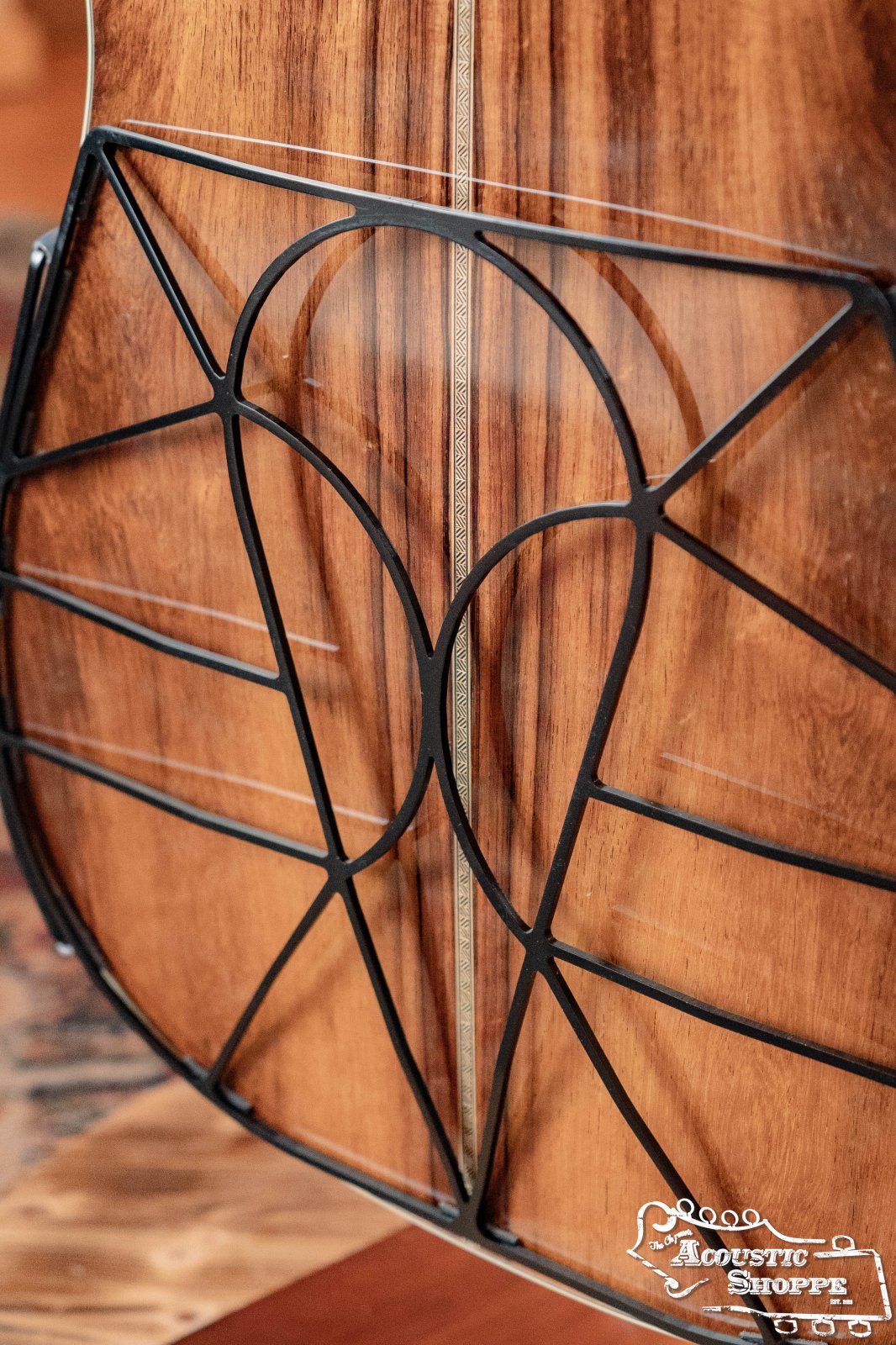 Close-up of a Tone-Gard Dreadnaught Guitar D-Gard by Tone-Gard on an acoustic guitars polished wooden back, featuring a black lattice cover and The Acoustic Shoppe logo in the corner. The wood has a decorative stripe to enhance tone.