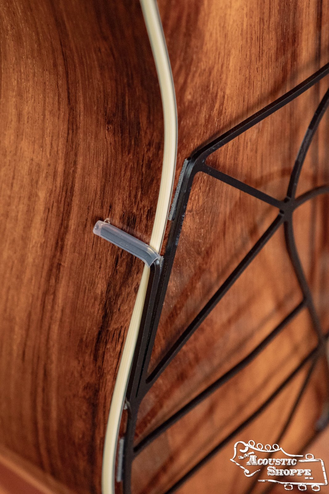 Close-up of a wooden guitar body with a black Tone-Gard Dreadnaught Guitar D-Gard by Tone-Gard, featuring cream binding, detailed wood grain, and a small plastic piece attached. The Acoustic Shoppe logo appears in the bottom right corner.