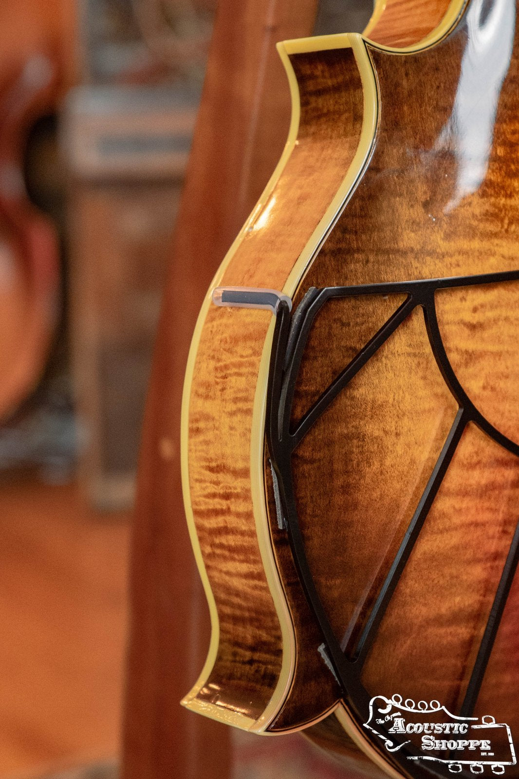 Close-up of the side and back of a glossy, wooden acoustic guitar with decorative binding, a black adjustable armrest, and the Tone-Gard Mandolin - Sunrise by Tone-Gard nearby. Acoustic Shoppe logo appears in the bottom right corner.