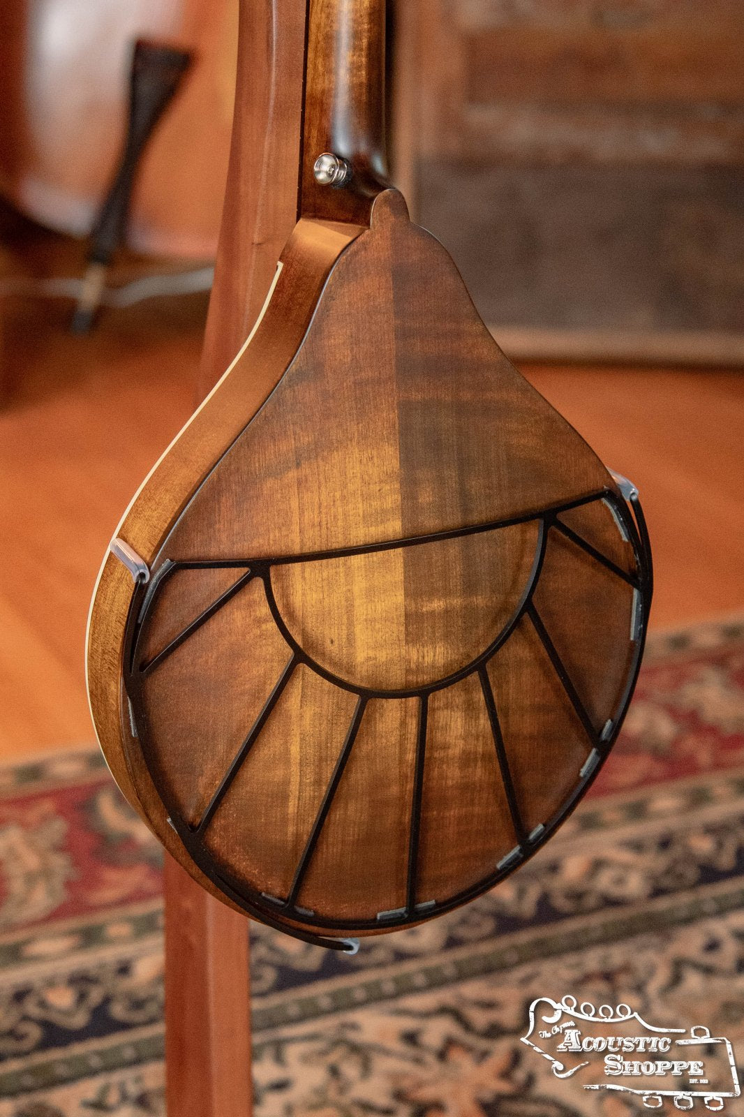 A close-up of the back of a mandolin with a unique sunburst pattern and black lines, fitted with the Tone-Gard Mandolin - Sunrise by Tone-Gard for added protection, and the Acoustic Shoppe logo in the corner.