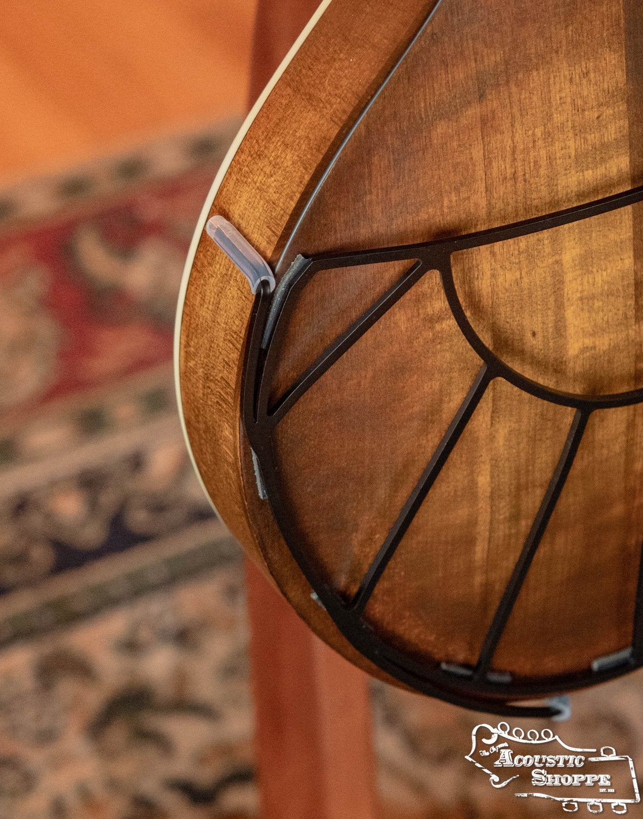 Close-up of a Tone-Gard Mandolin - Sunrise back protector by Tone-Gard fitted on a stringed instrument, with a geometric black soundhole cover and part of the Acoustic Shoppe logo visible; a patterned rug appears in the background.