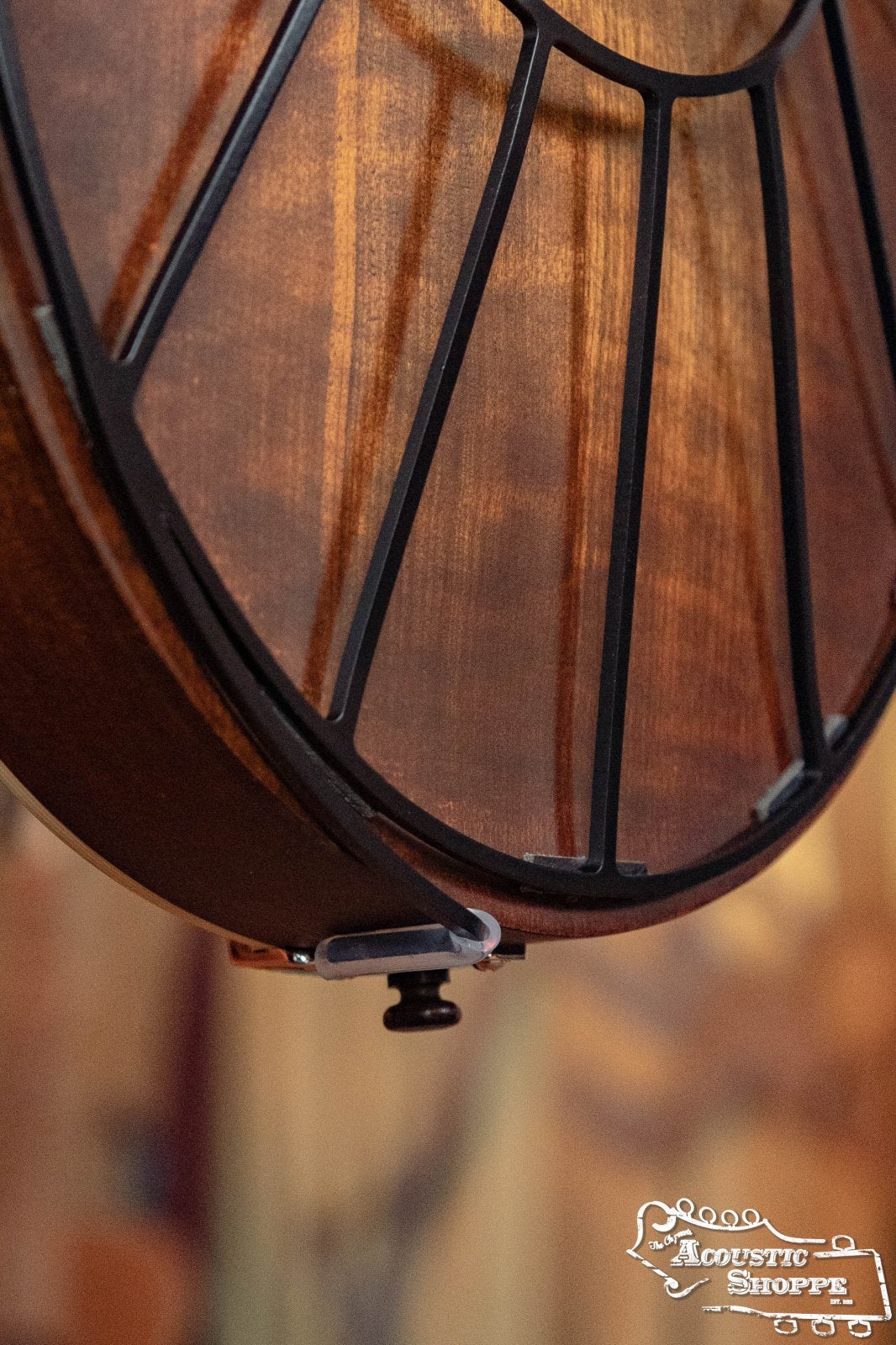 Close-up of a Tone-Gard Mandolin - Sunrise by Tone-Gard fitted on a wooden mandolin body, highlighting the circular metal frame and wood grain. A black strap button is seen at the bottom. Acoustic Shoppe logo in lower right corner.