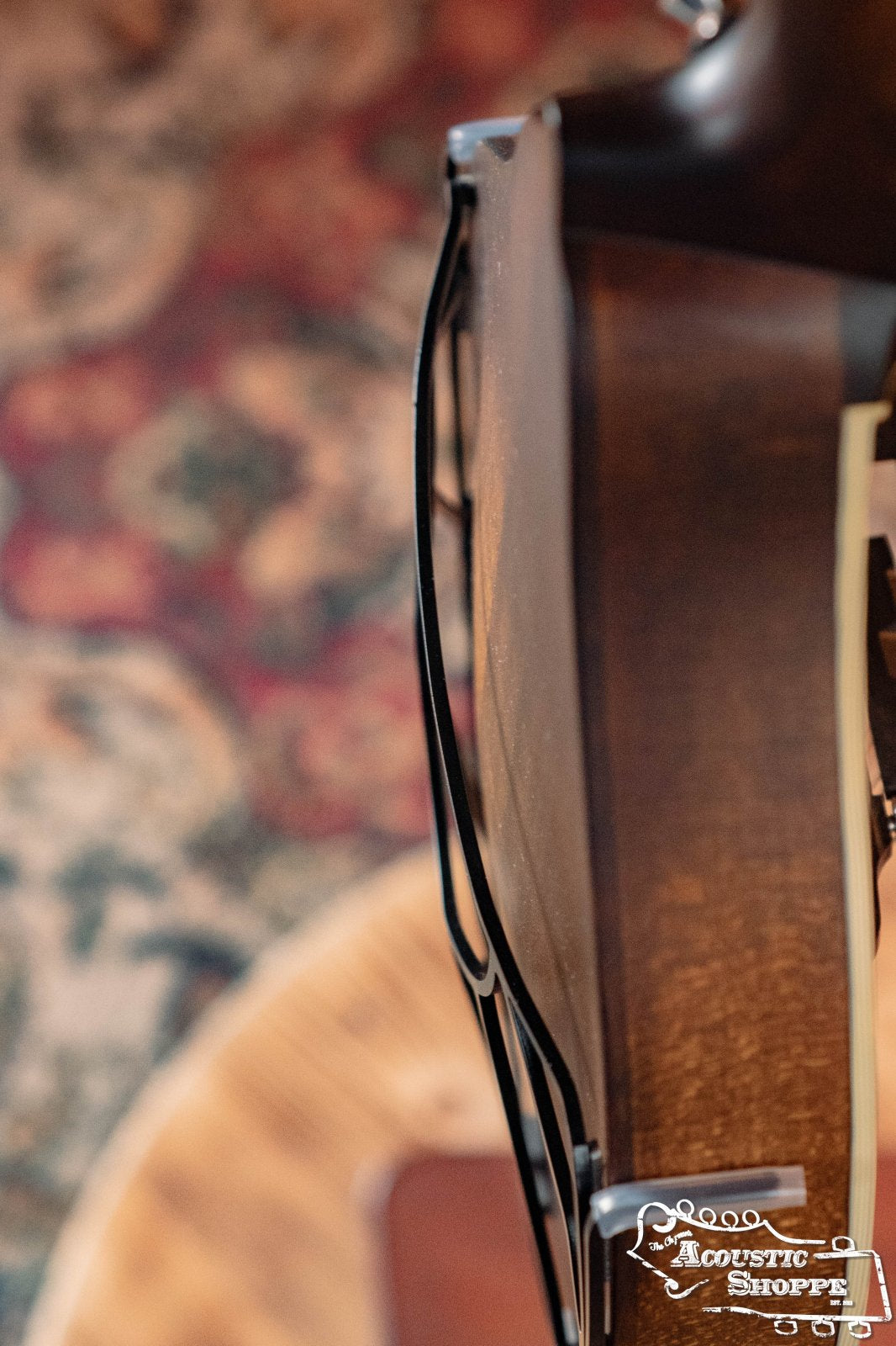 Side view of a mandolin with the Tone-Gard Mandolin - Vintage by Tone-Gard attached, showing wood grain and part of a patterned rug in the background. Acoustic Shoppe logo is visible in the lower right corner.