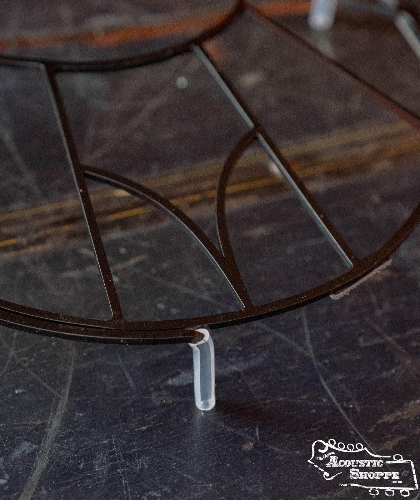 A close-up of the Tone-Gard Mandolin - Vintage by Tone-Gard, a round black metal frame with thin rods, displayed on clear plastic stands atop a dark surface. The Acoustic Shoppe logo is shown as an instrument back protector.