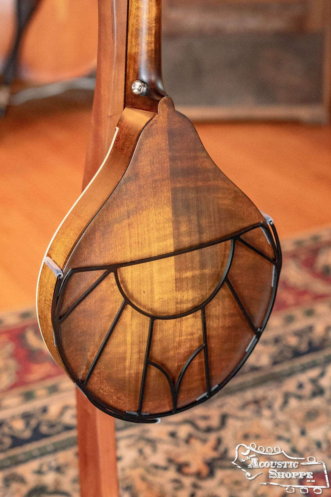 A close-up of a Tone-Gard Mandolin - Vintage by Tone-Gard, a decorative black metal grid enhancer and back protector attached to the back of a mandolin. A patterned rug and wooden floor are visible in the background.