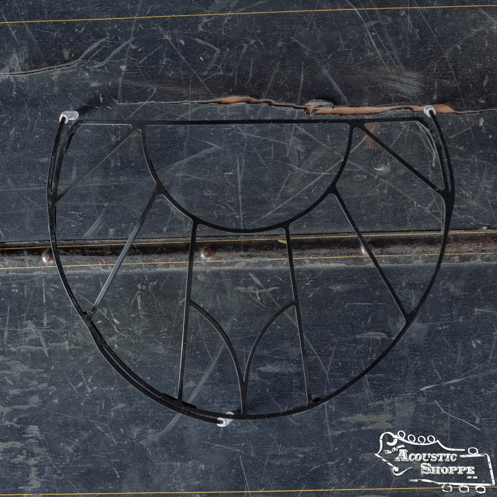 A black, semi-circular Tone-Gard OM-Gard Octave Mandolin pickguard by Tone-Gard with geometric cutouts rests on a scratched, dark wood surface. The Acoustic Shoppe logo is in the lower right corner. Perfect for subtly enhancing mandolin tone.