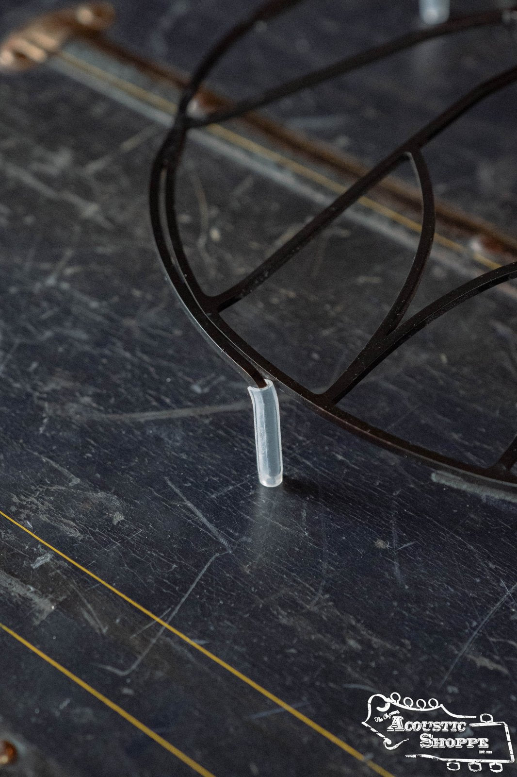 A close-up of the Tone-Gard OM-Gard Octave Mandolin accessory by Tone-Gard, featuring a black metal circular frame with a clear plastic protector, resting on a scratched dark surface. The Acoustic Shoppe logo is visible in the lower right corner.