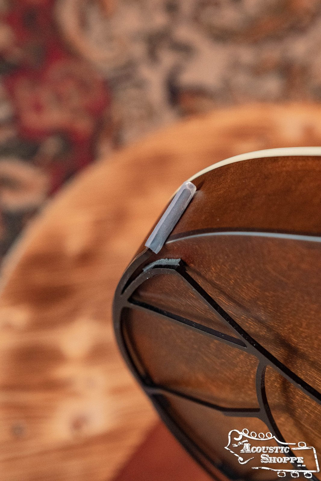 Close-up of a Tone-Gard OM-Gard Octave Mandolin by Tone-Gard, highlighting wood grain, binding, and detailing. The Acoustic Shoppe logo and a blurred patterned rug appear in the background.
