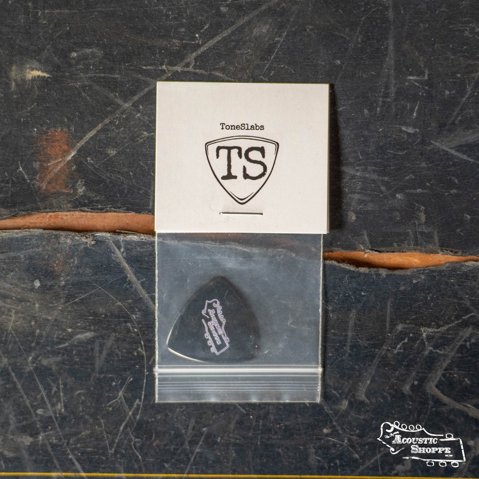 A ToneSlabs Darth Tone Series Tri Micro 1.2mm guitar pick in black is in a small plastic bag on a worn dark surface, with a ToneSlabs logo card above and the Acoustic Shoppe logo at the bottom right.