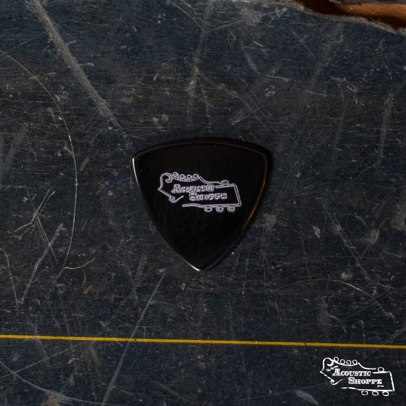 A ToneSlabs Darth Tone Series Tri Micro 1.2mm pick in black, featuring a white Acoustic Shoppe logo, rests on a scratched dark surface. The Acoustic Shoppe logo also appears in the lower right corner of the image.
