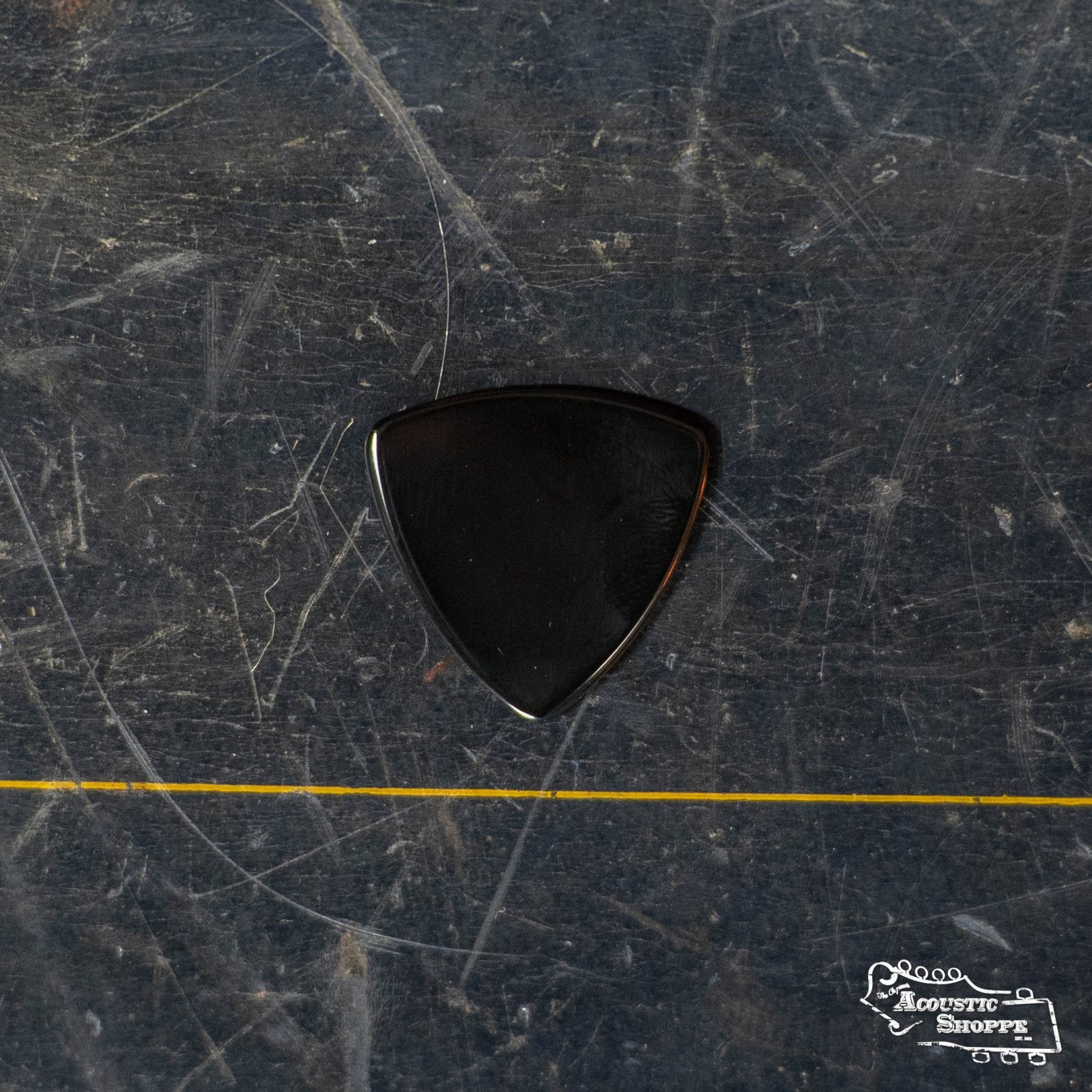 A ToneSlabs Darth Tone Series Tri Micro 1.5mm black guitar pick sits on a scratched, dark surface with a thin yellow line at the bottom. The Acoustic Shoppe logo appears in the lower right, showcasing this compact accessory for musicians.