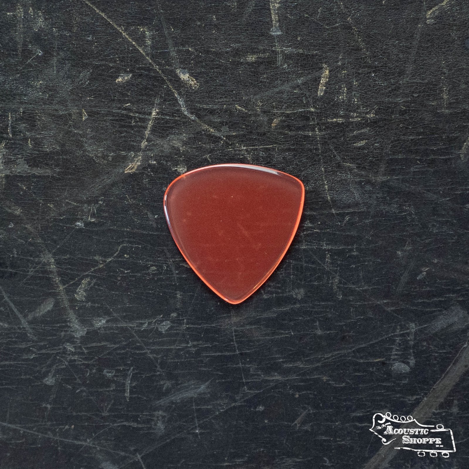 A single ToneSlabs Mini Tri 1Round Guitar Pick - 1.2mm in reddish-brown, shaped like a standard triangle with a glossy finish, lies on a black scratched surface. The Acoustic Shoppe logo appears in the lower right corner.