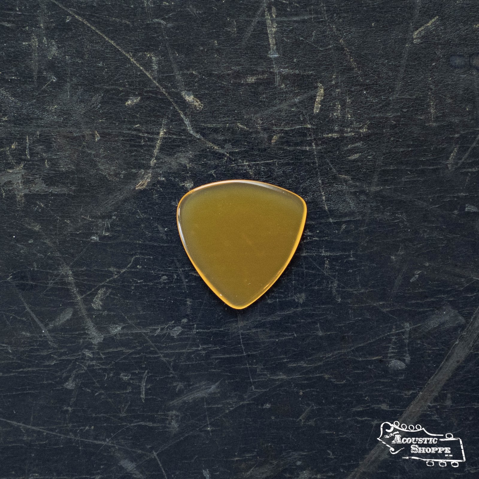 A ToneSlabs Mini Tri 1Round Guitar Pick - 1.5mm by ToneSlabs sits on a dark, scratched surface, with an “Acoustic Shoppe” logo in the corner—a top pick for acoustic guitar accessories.