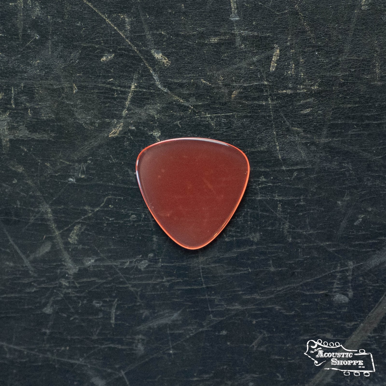 A ToneSlabs Mini Tri 3Round Guitar Pick - 1.2mm by ToneSlabs rests on a worn black surface, with The Acoustic Shoppe logo in white at the bottom right.