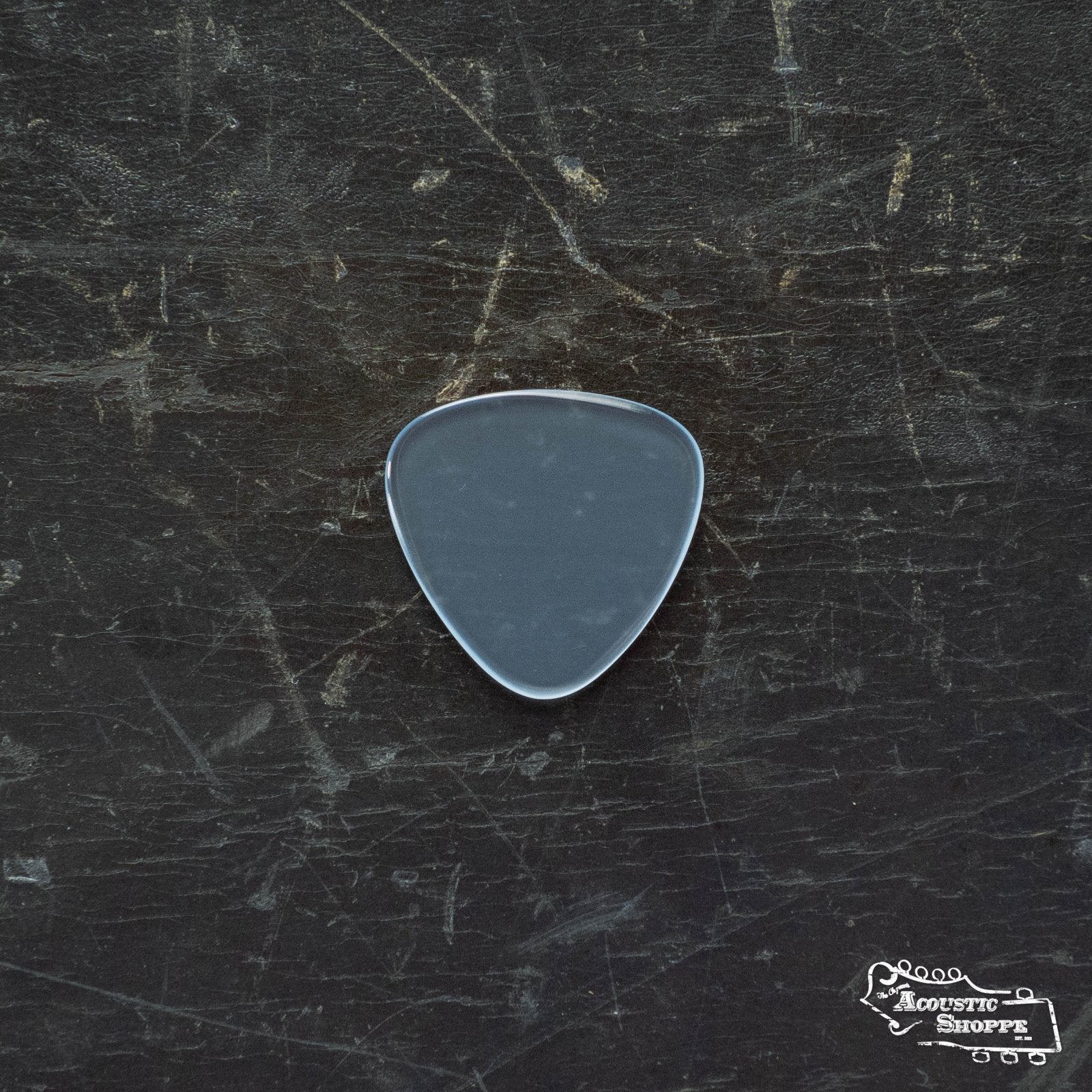 A single gray ToneSlabs Mini Tri 3Round Guitar Pick - 1.4mm rests on a scratched, dark surface, with The Acoustic Shoppe logo in white at the bottom right. Ideal for precision and clarity.
