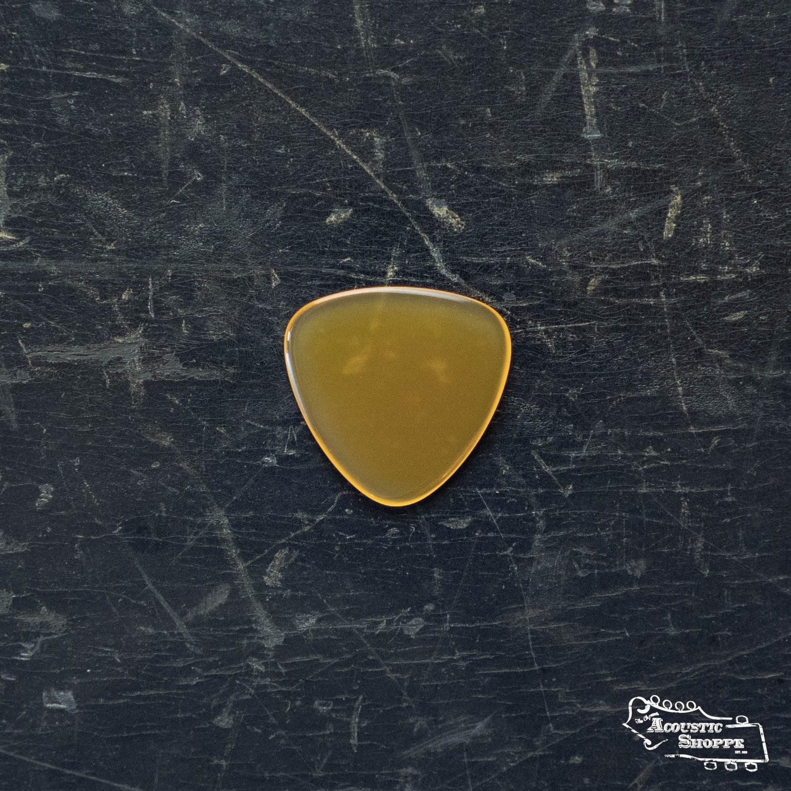 A ToneSlabs Mini Tri 3Round Guitar Pick - 1.5mm in brown lies on a scratched black surface, with the white Acoustic Shoppe logo visible in the lower right corner.