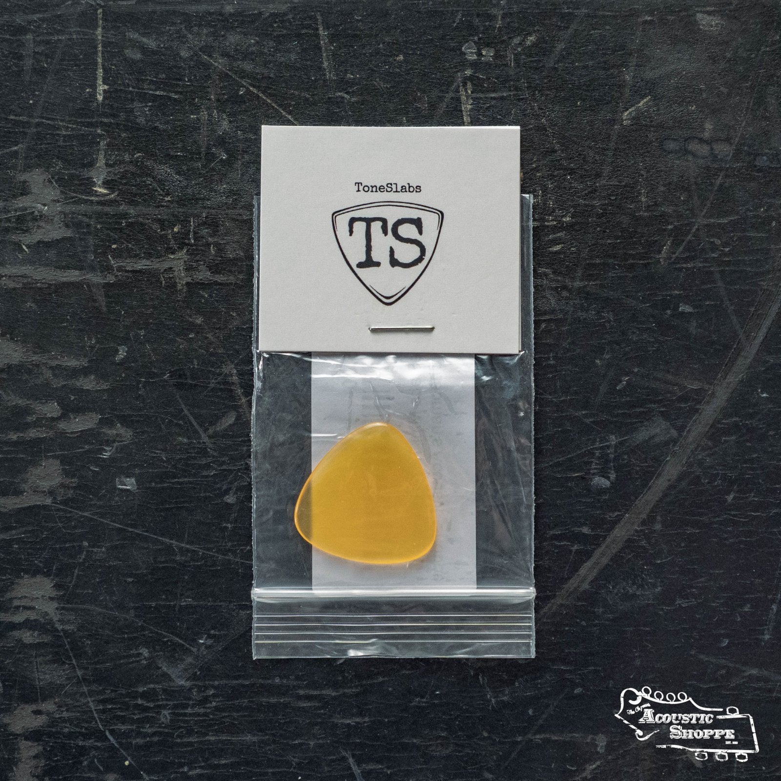 A ToneSlabs Mini Tri 3Round Guitar Pick (1.5mm) in yellow is shown in a small plastic bag on a dark surface, with a white ToneSlabs card above it and The Acoustic Shoppe logo at the bottom right.