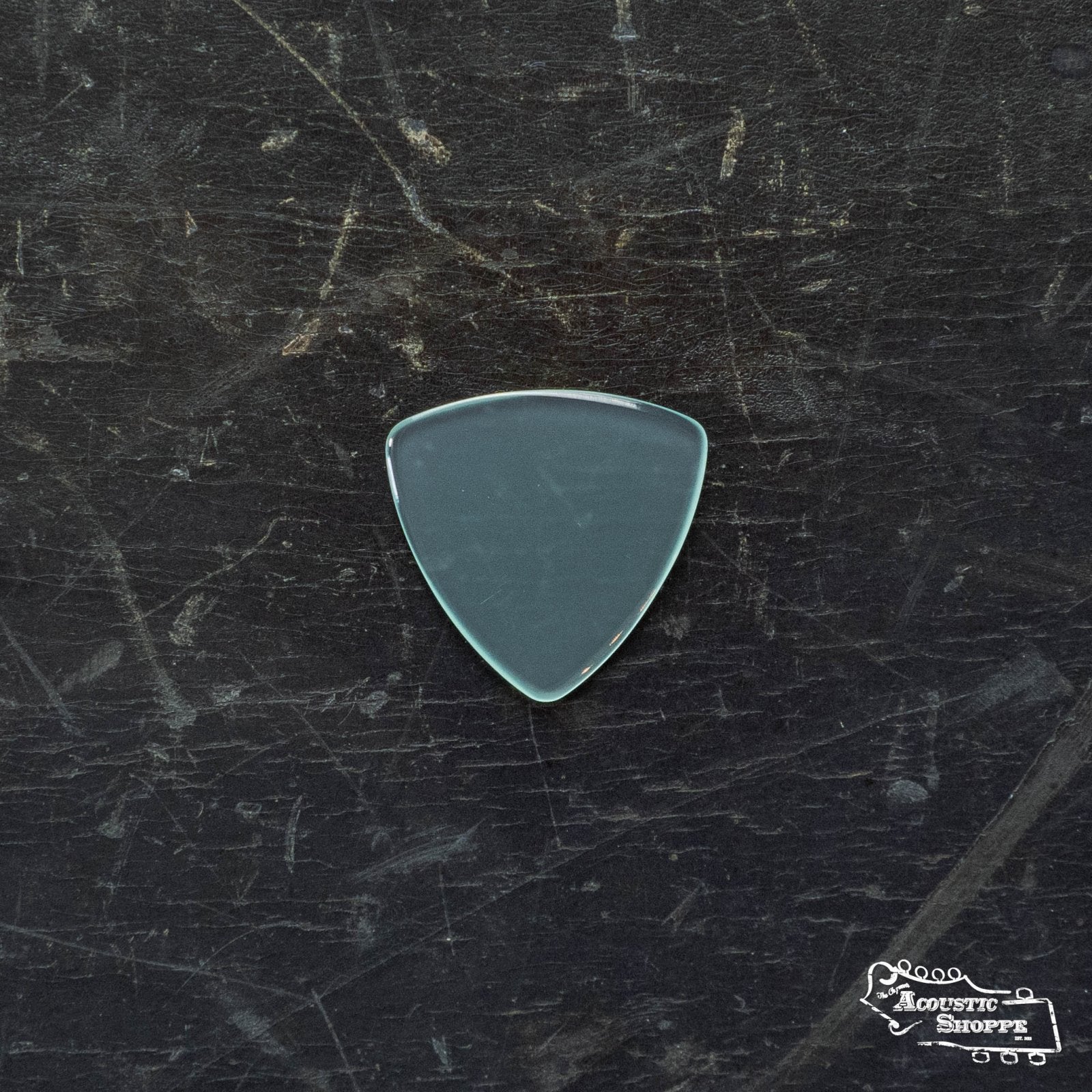 A ToneSlabs TAS Custom Mini Tri Guitar Pick - 1.3mm (Exclusive Color) rests on a scratched dark surface, with a small Acoustic Shoppe logo visible in the lower right corner.