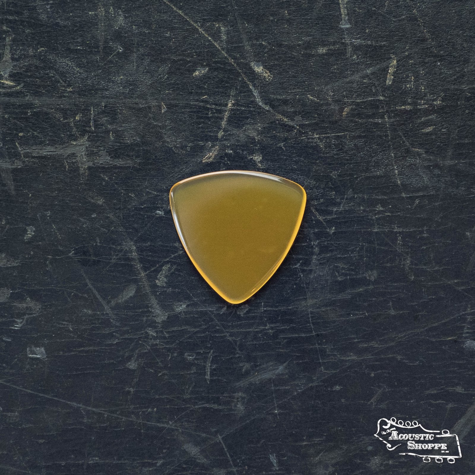 A ToneSlabs Mini Tri Guitar Pick - 1.5mm by ToneSlabs rests on a worn, scratched black surface. The brown, triangular pick features smooth corners, and a small white logo appears in the lower right background.