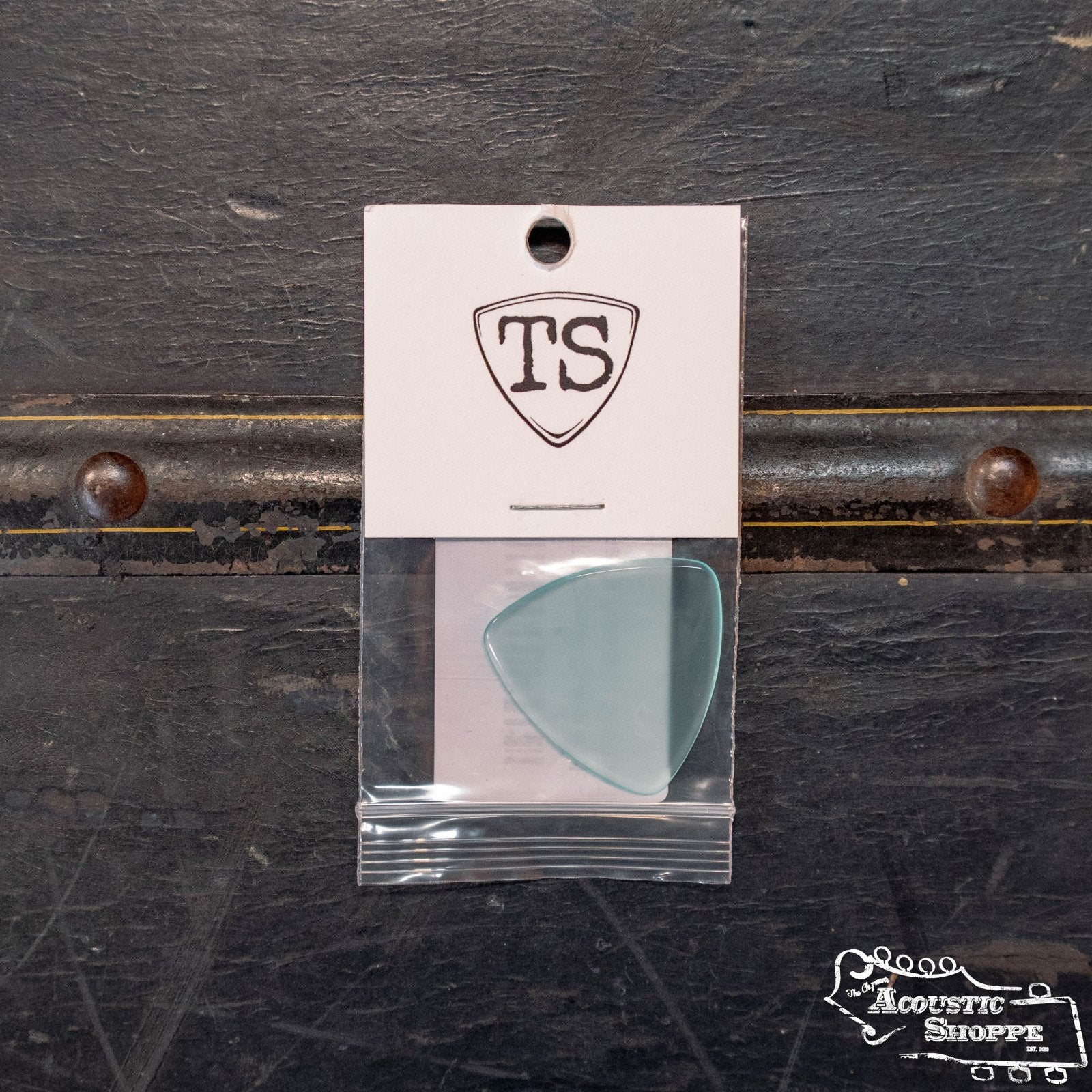 A ToneSlabs TAS Custom XL Tri Corner Guitar Pick (1.3 mm, exclusive light blue, signed) sits in a clear bag on a white card with the TS logo atop dark metal. The Acoustic Shoppe logo is in the corner, showcasing its premium tonal quality.