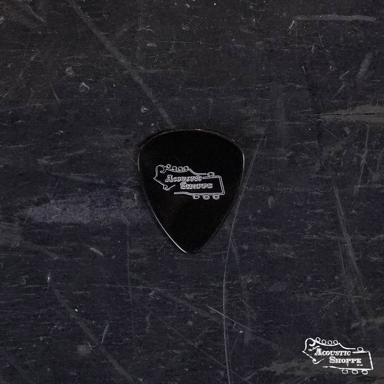 A ToneSlabs Darth Tone Series Tear Drop Guitar Pick (1.2 mm, black) with the Acoustic Shoppe logo in white rests on a dark, scratched surface; the same logo is also in the image’s lower right corner.