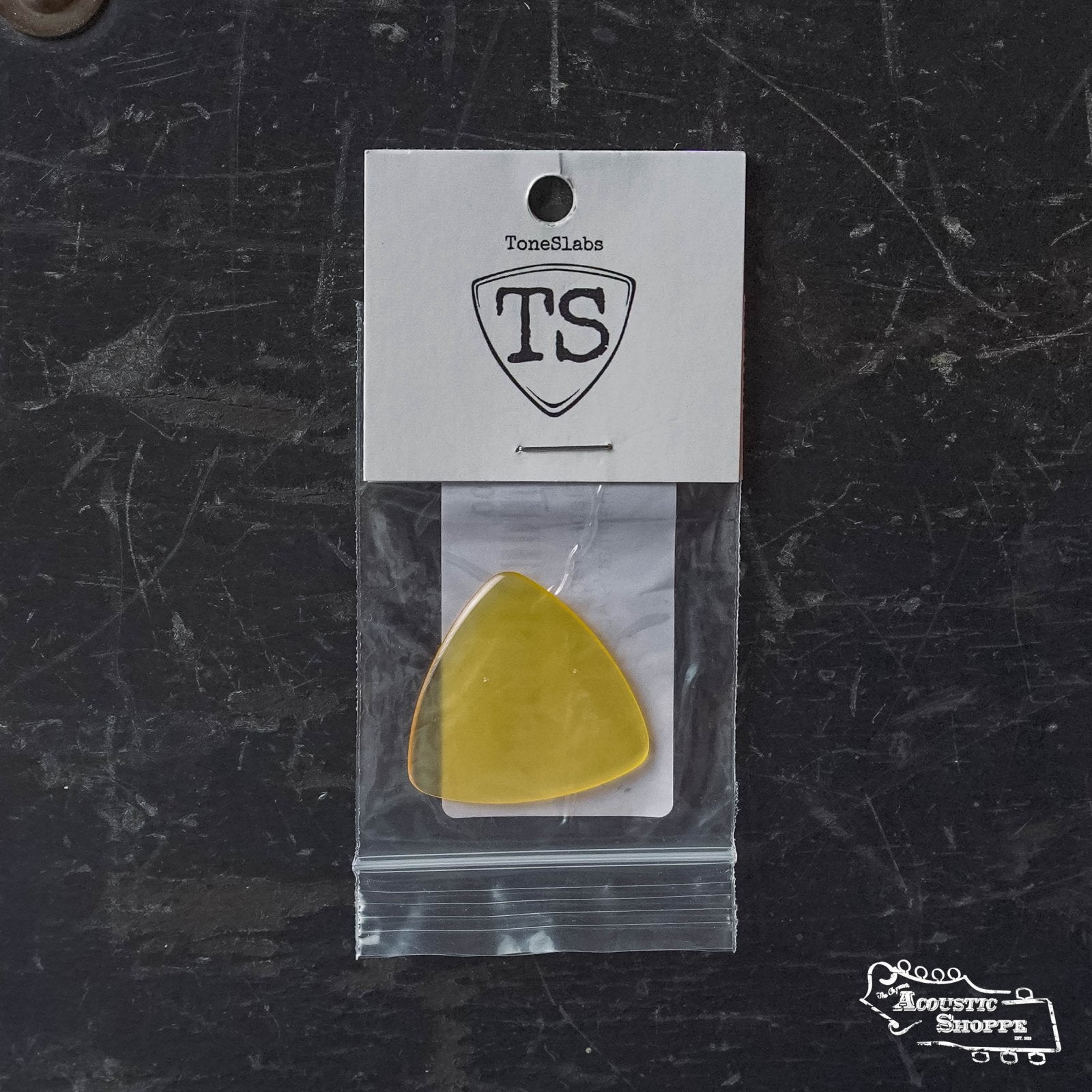 A ToneSlabs Frank Solivan Guitar Pick 1.5, yellow, in a clear zip bag with white label on a dark textured surface featuring The Acoustic Shoppe logo—ideal for those looking for boutique guitar accessories.