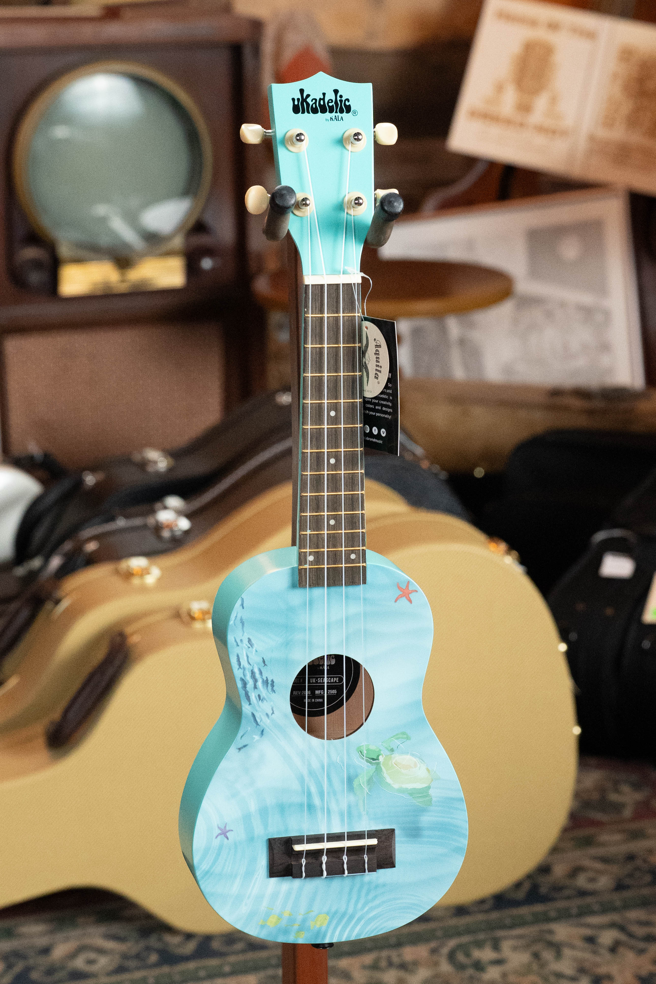 Light blue soprano ukulele with seascape design and dark fretboard, standing in front of a tan hard case. - Ukadelic Seascape Soprano Ukulele - Kala Brand - Default Title