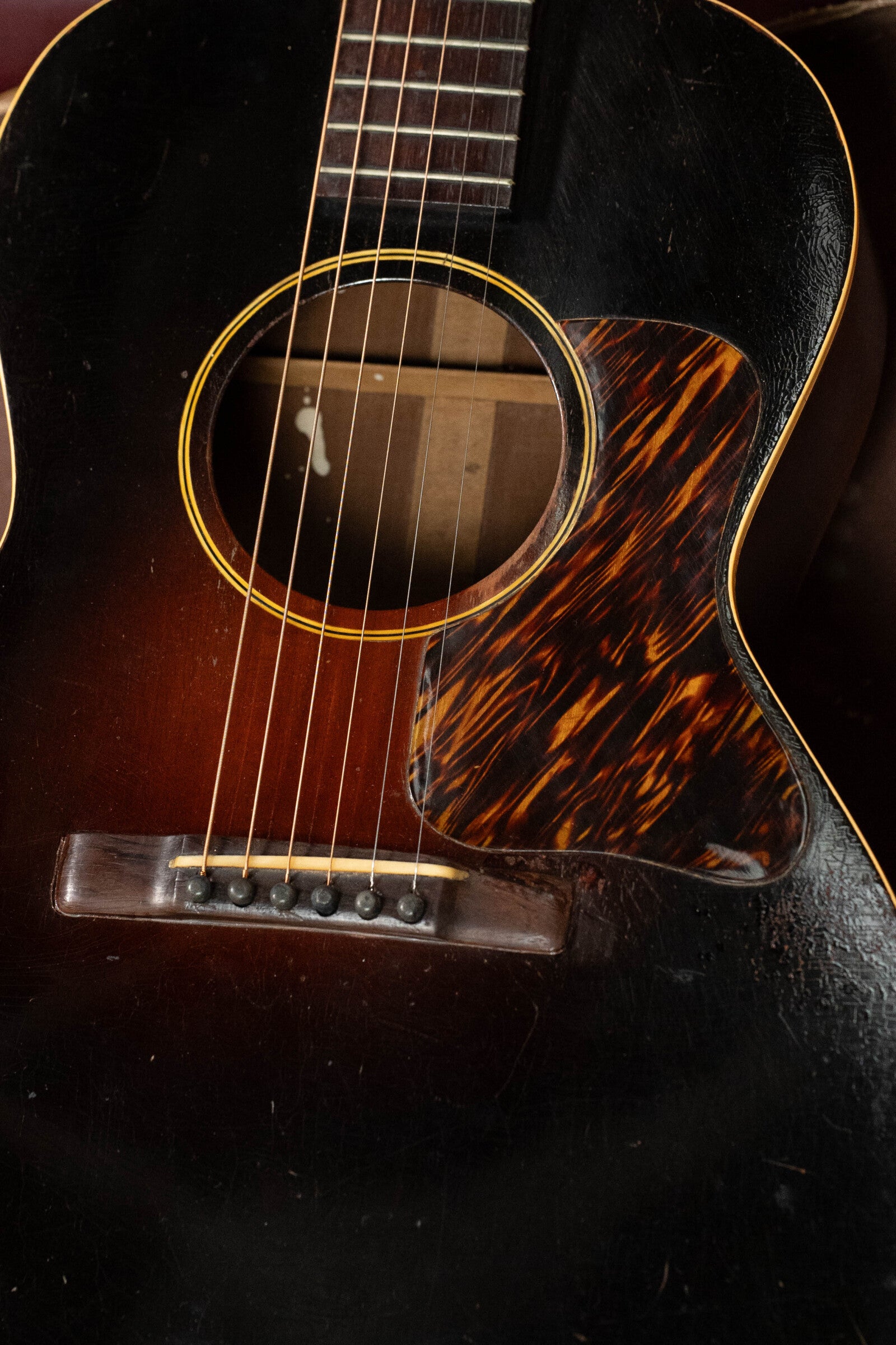 Close-up of a (Used) 1933 Gibson LOO Adirondack/Mahogany OO Tobacco Sunburst Acoustic Guitar #550, featuring its sunburst finish, six strings, tortoiseshell pickguard, visible wood grain, Adirondack spruce top, sound hole, and bridge.