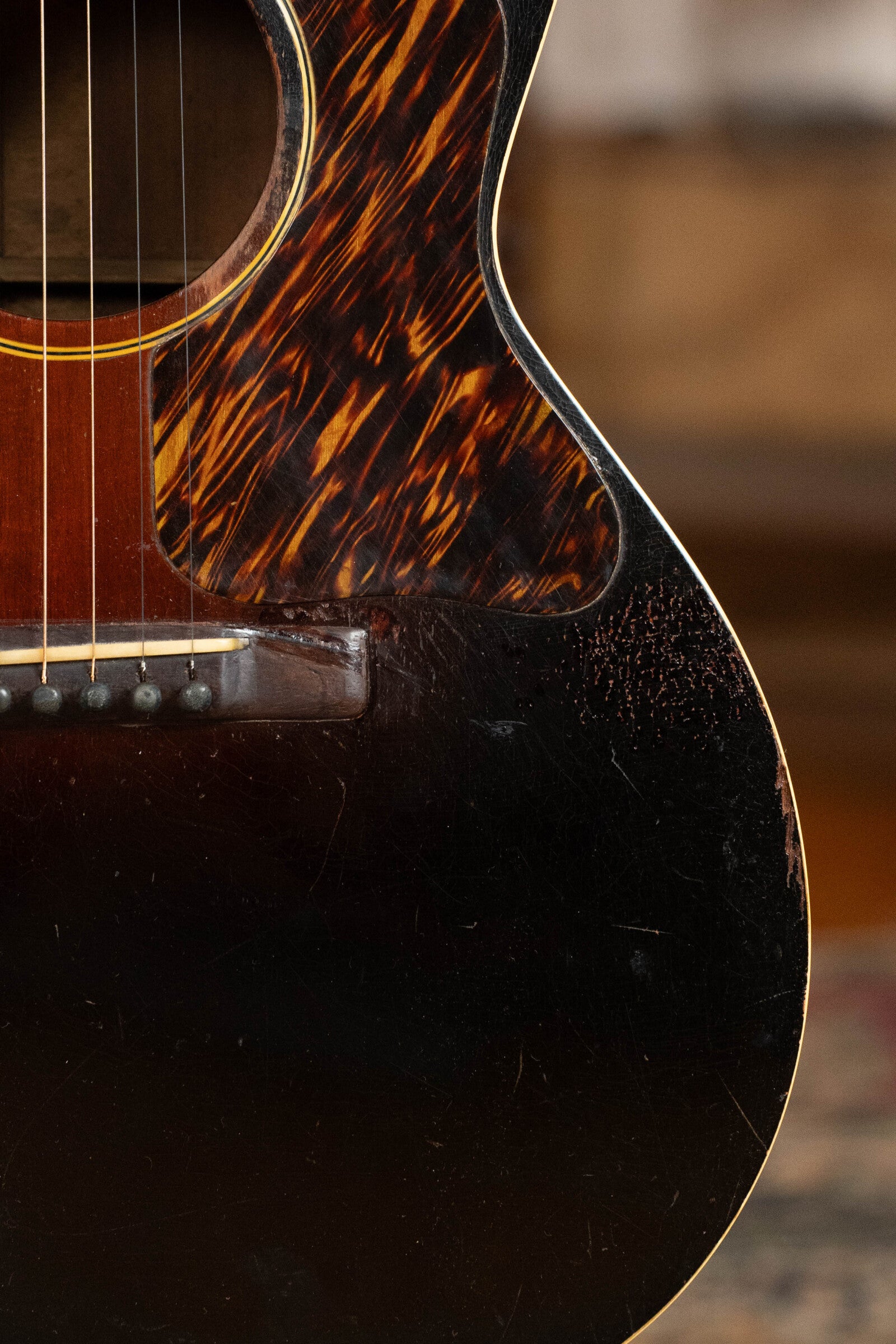 Close-up of a used 1933 Gibson LOO Adirondack/Mahogany OO Tobacco Sunburst Acoustic Guitar #550, featuring its Adirondack spruce top, tortoiseshell pickguard, visible strings, and worn dark finish. Brand: Gibson.