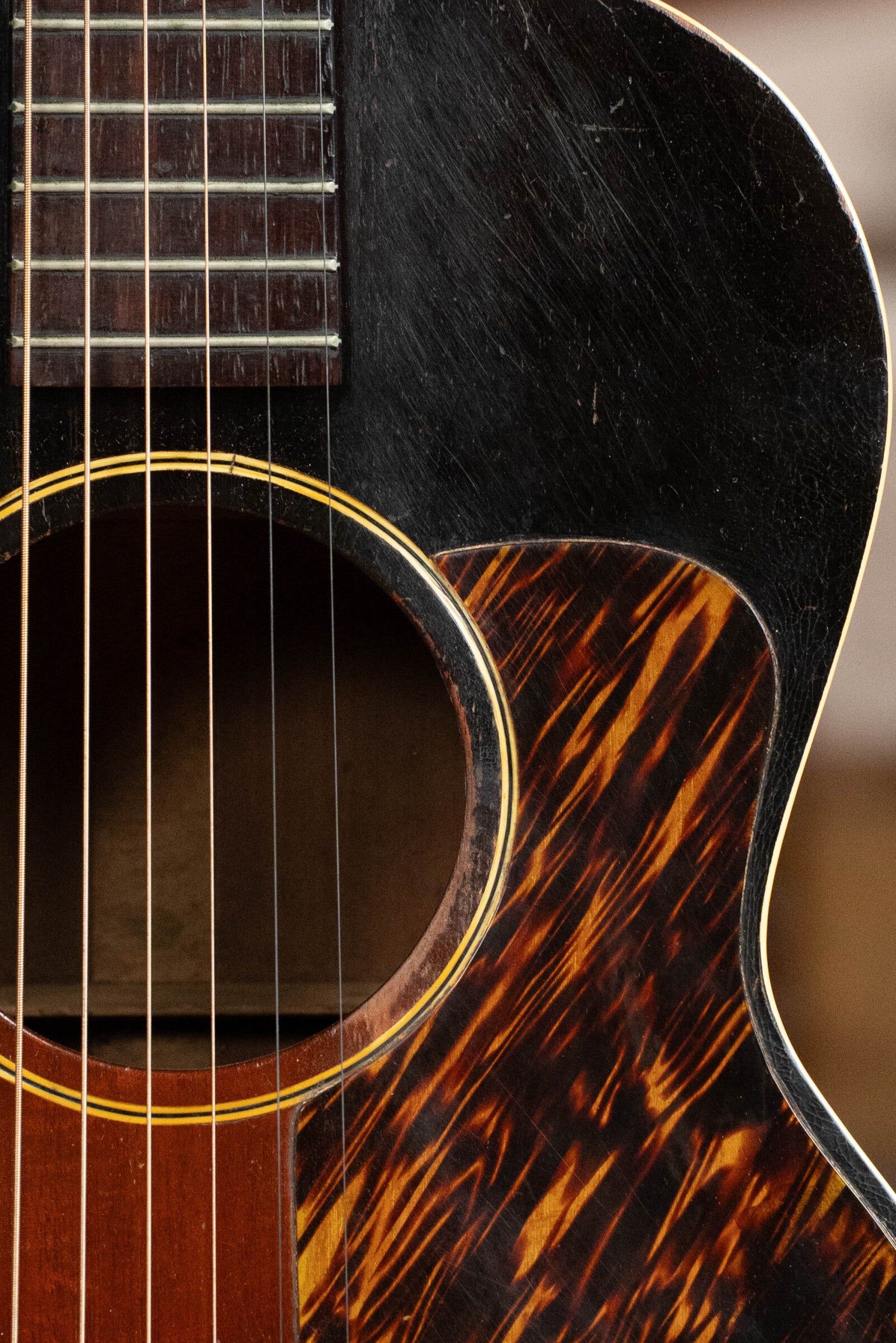 Close-up of a (Used) 1933 Gibson LOO Adirondack/Mahogany OO Tobacco Sunburst Acoustic Guitar #550 by Gibson, detailing its strings, sound hole, fretboard, tortoiseshell pickguard, and worn Adirondack spruce top.