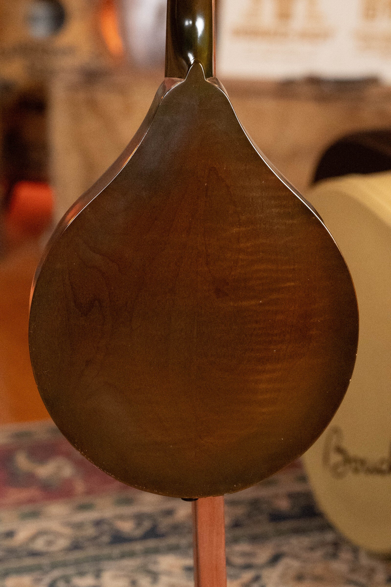 Close-up of the back of a (Used) 2003 Gibson Mastermodel A9 Spruce/Maple Mandolin #7040, with a polished finish. A patterned rug and blurred objects in the background evoke a warm bluegrass feel. Brand: Gibson.