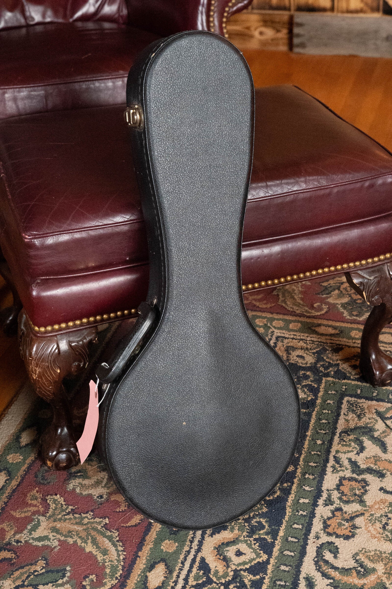 A used 2003 Gibson Mastermodel A9 Spruce/Maple Mandolin (#7040) in its black hard-shell case stands upright by a leather armchair on a patterned rug, ready for your next bluegrass jam.