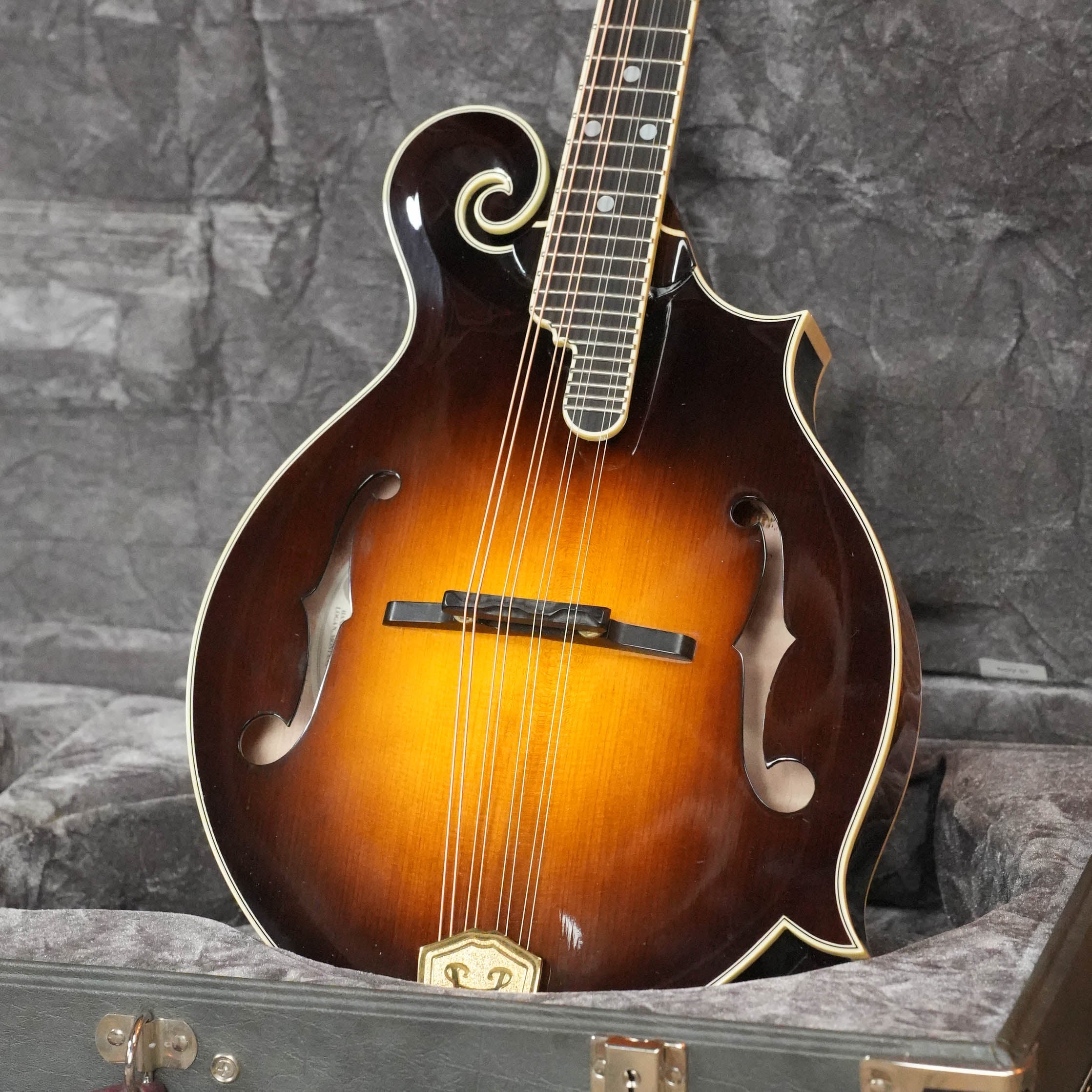 A close-up of a (Used) 2009 Weber Fern Spruce/Maple F-Style Mandolin #7602, featuring intricate scrollwork and set in a gray-lined hard case against a dark backdrop—a stunning example from Weber.